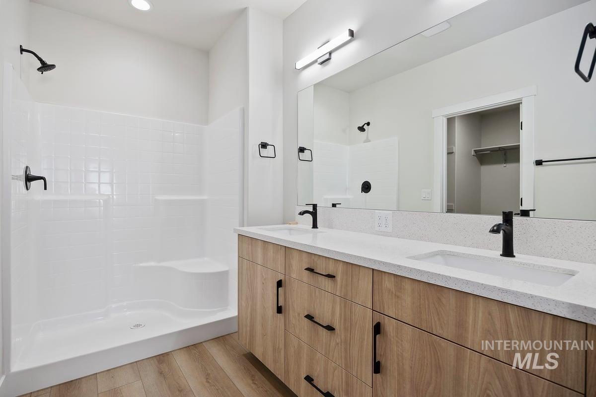 Bathroom featuring light wood finished floors, double vanity, a walk in closet, and a shower