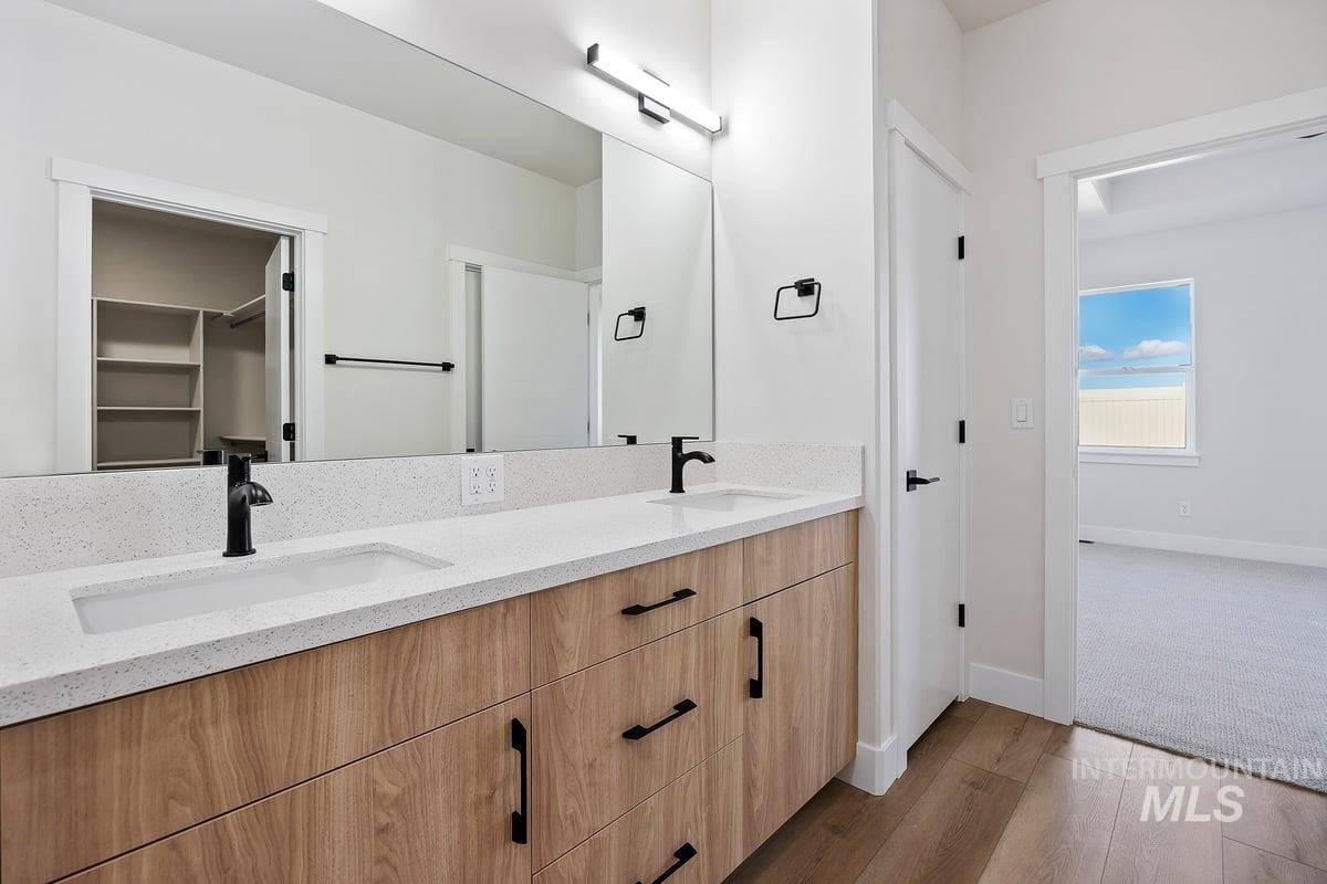 Full bathroom with dark wood-type flooring, double vanity, and a spacious closet