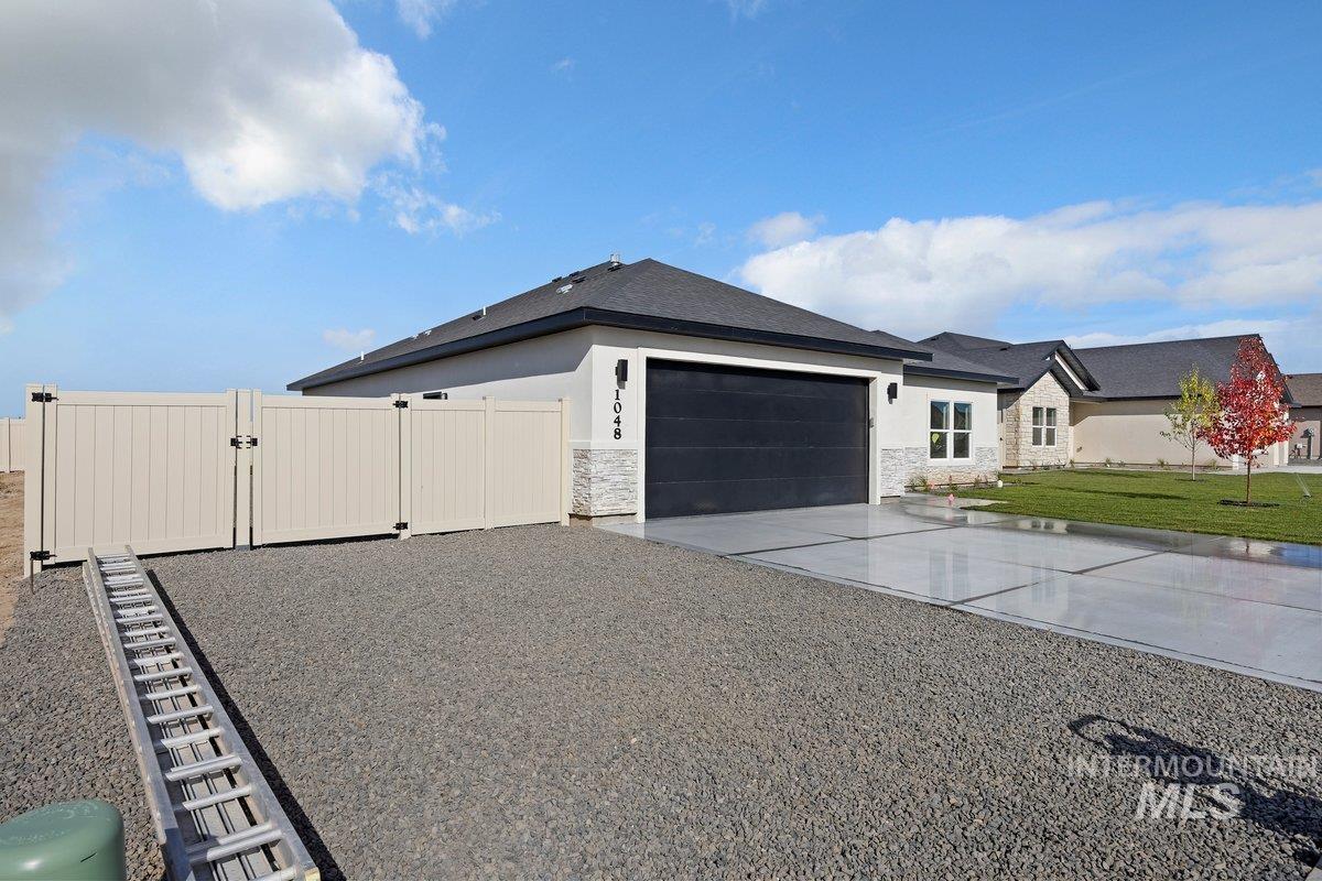 View of side of home featuring a gate, concrete driveway, an attached garage, stone siding, and stucco siding