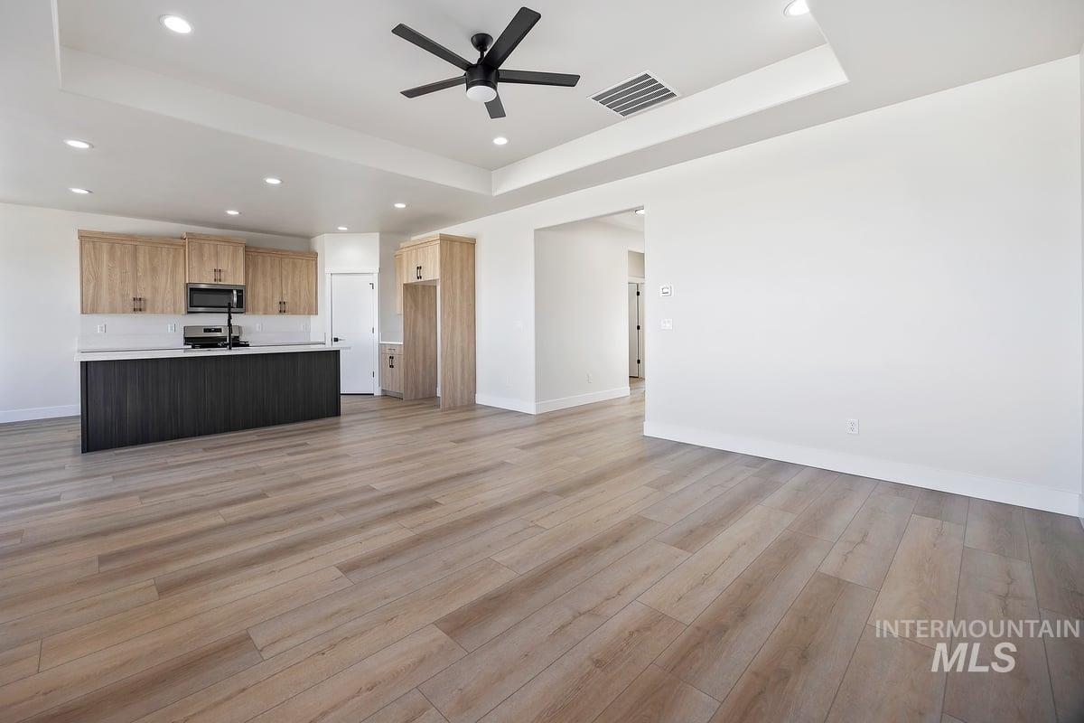 Unfurnished living room with a raised ceiling, light wood-style flooring, recessed lighting, and ceiling fan