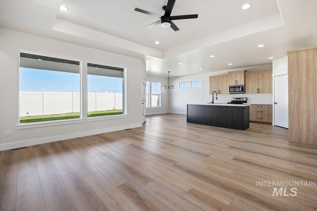 Unfurnished living room featuring a tray ceiling, ceiling fan, light wood-style floors, and recessed lighting