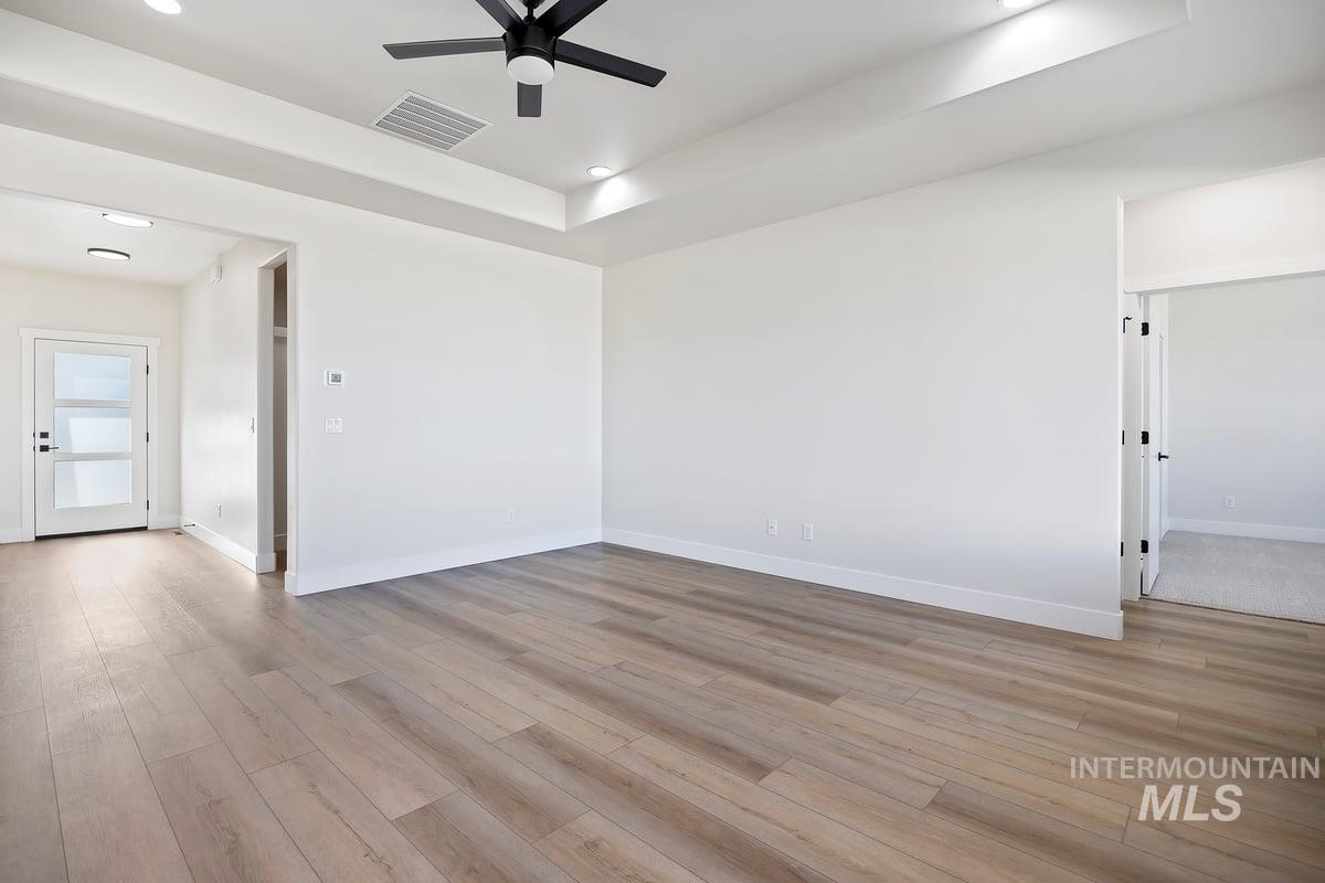 Unfurnished room with a raised ceiling, light wood-style flooring, a ceiling fan, and recessed lighting