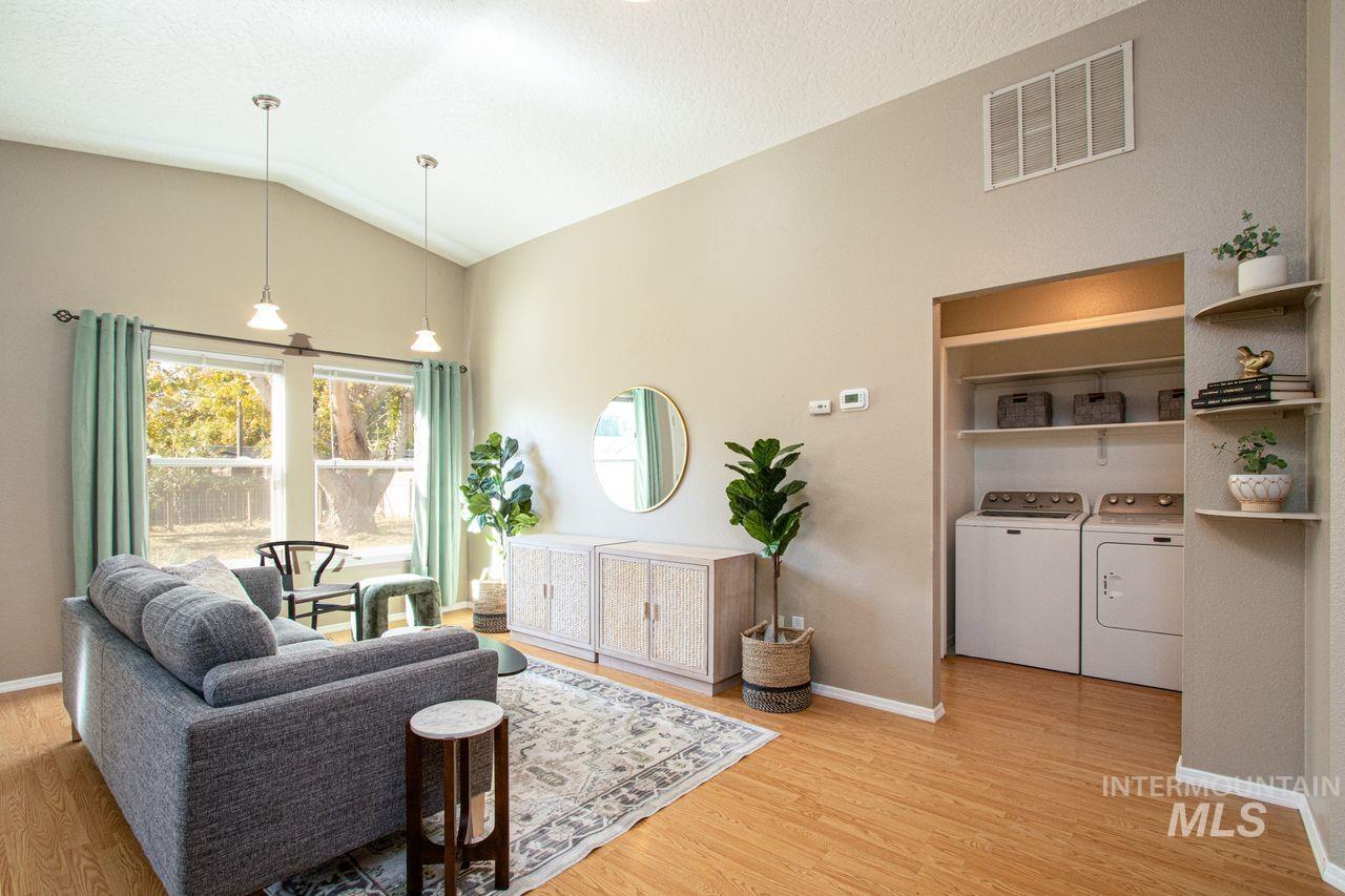 Living room with independent washer and dryer, light wood-style floors, and lofted ceiling
