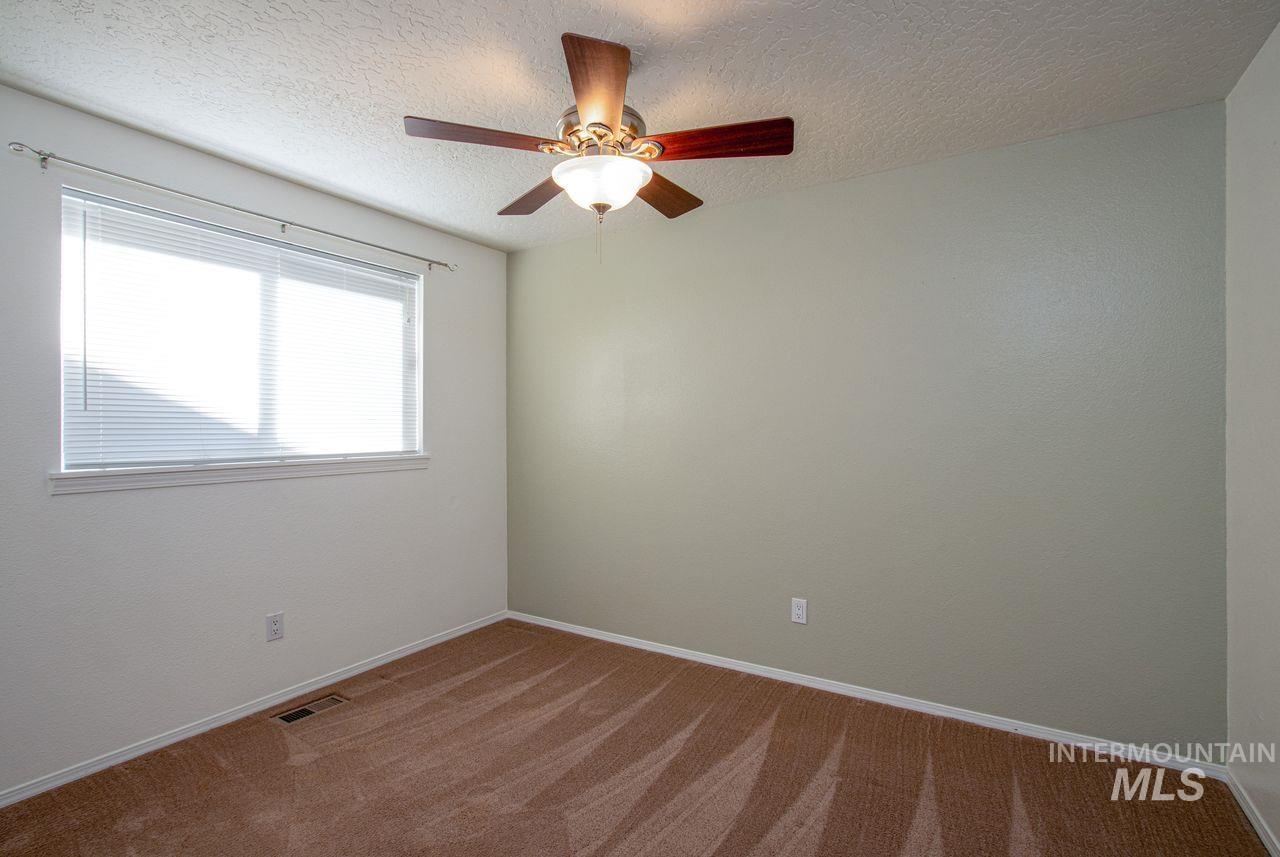 Carpeted empty room with a textured ceiling and ceiling fan