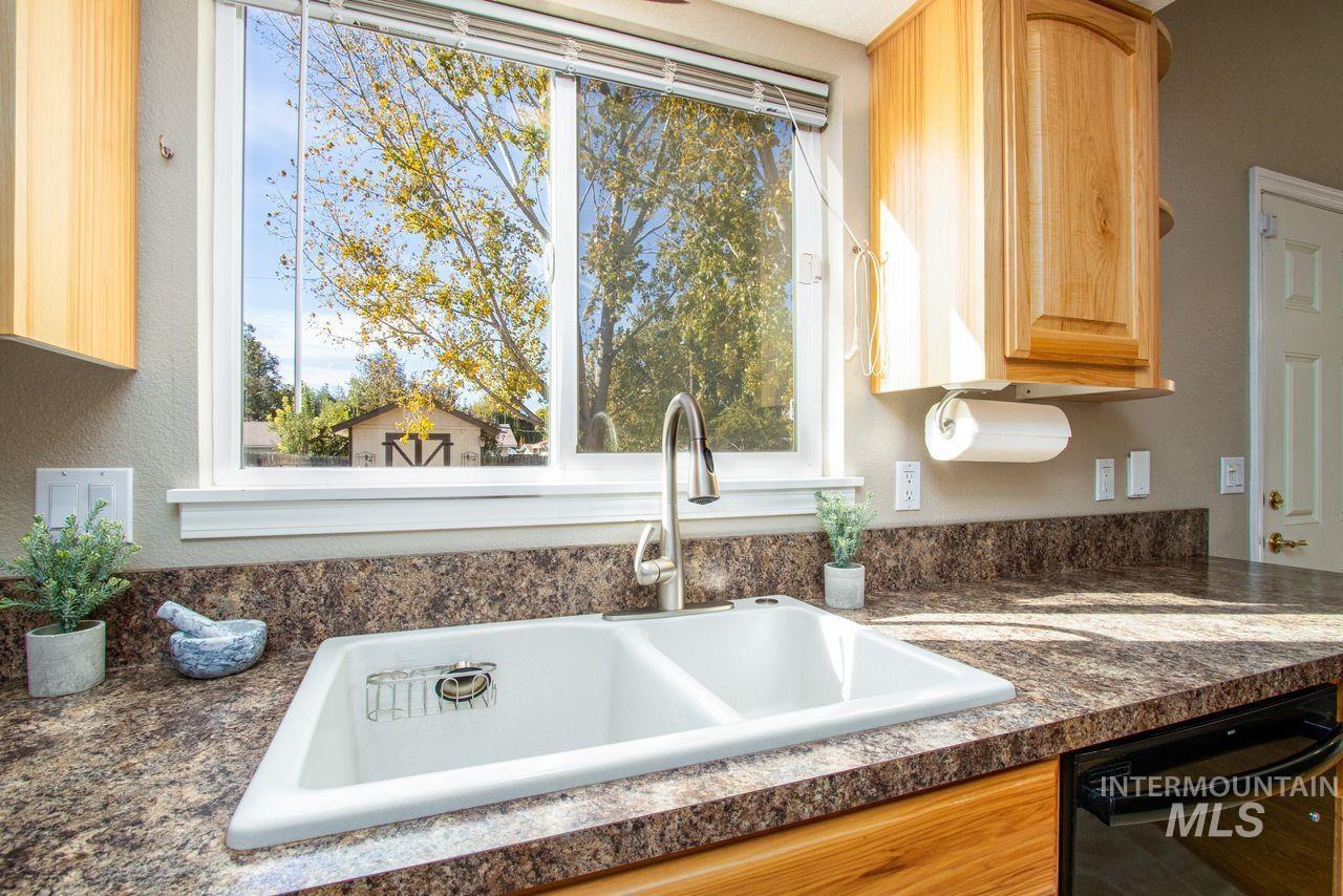 Kitchen view of dark countertops, black dishwasher, a textured wall, and light brown cabinetry