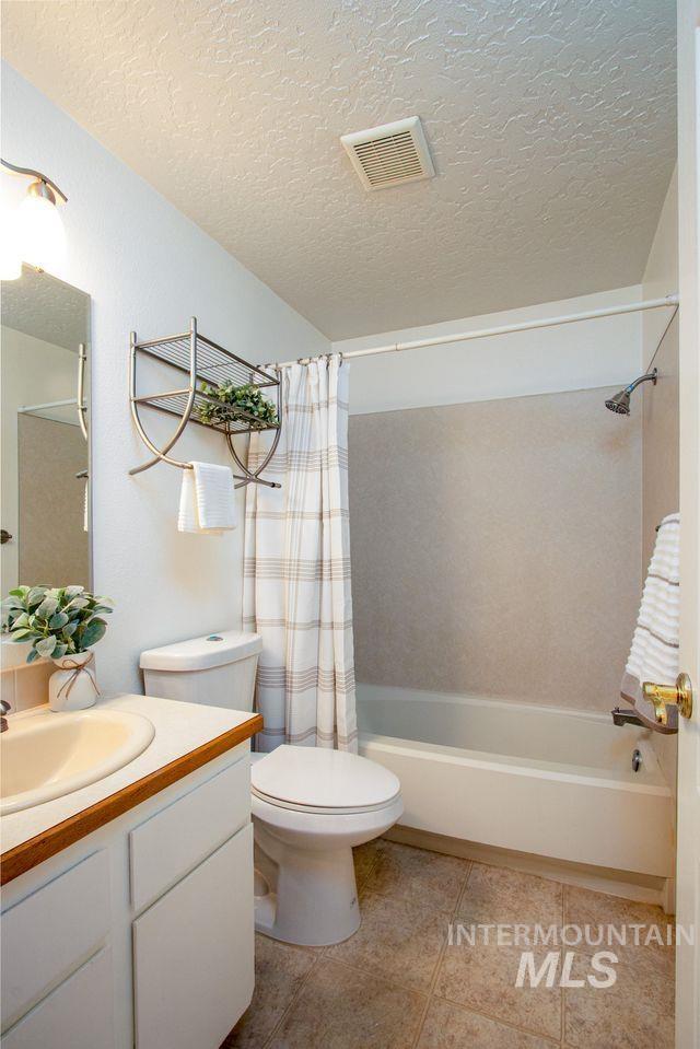 Bathroom featuring vanity, a textured ceiling, shower / tub combo with curtain, and light tile patterned floors
