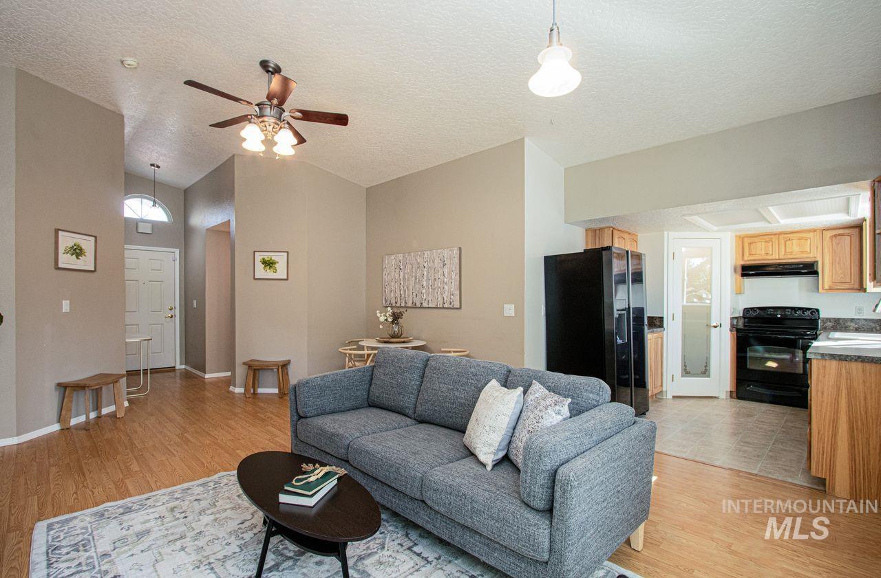 Living area featuring a textured ceiling, light wood-style floors, ceiling fan, and lofted ceiling