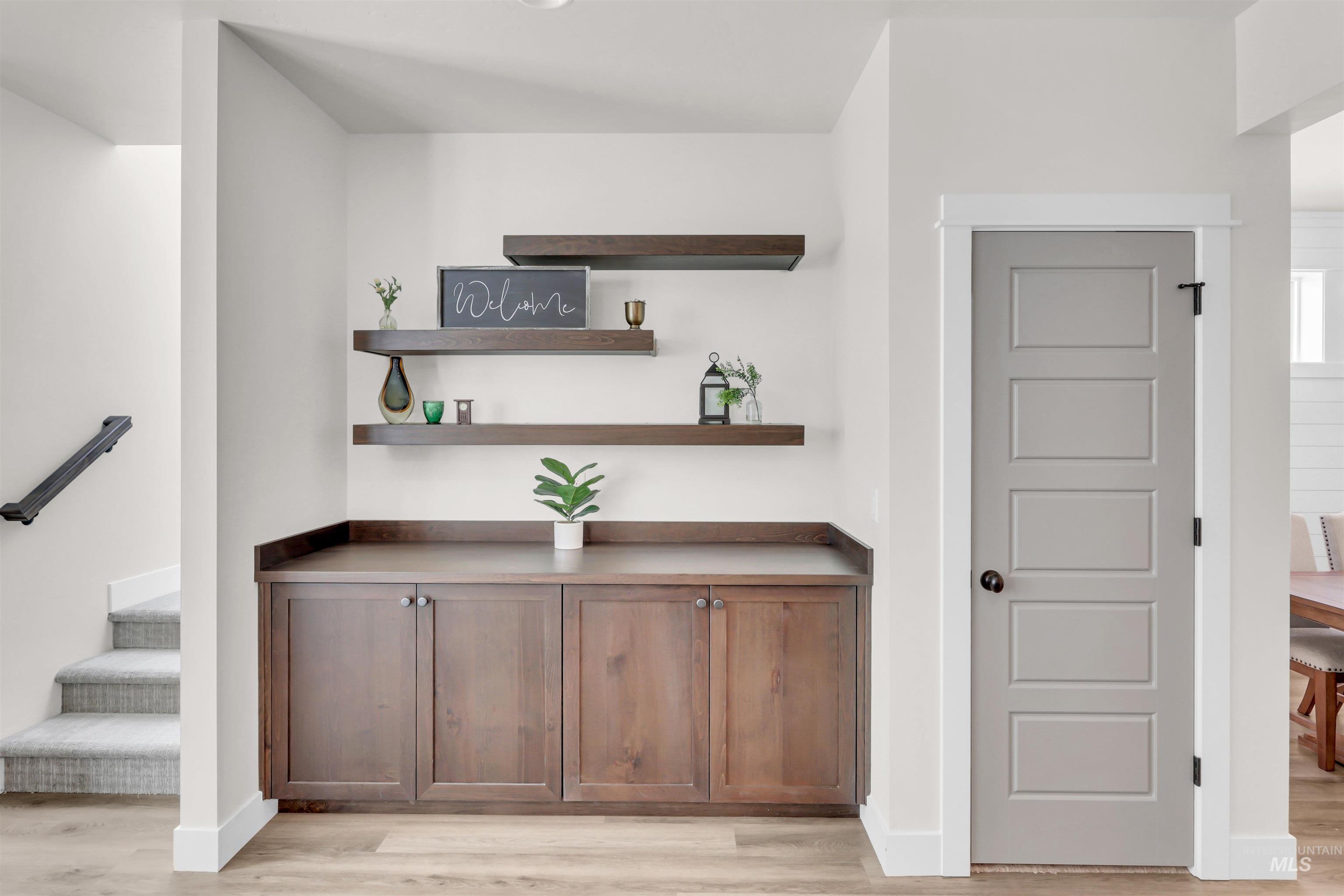 Bar area with light wood-style flooring, open shelves, stairway, and dark countertops
