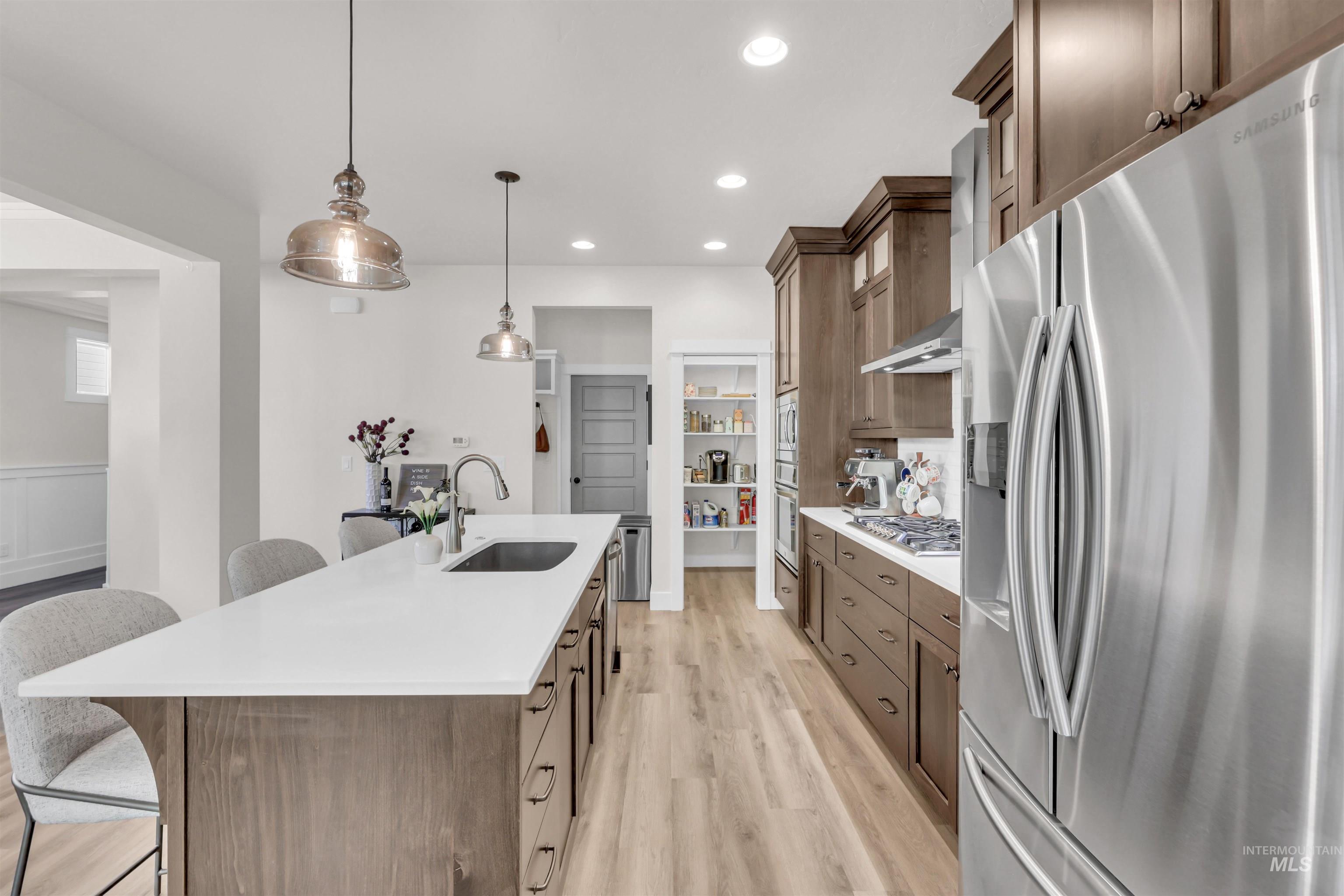 Kitchen featuring appliances with stainless steel finishes, a breakfast bar area, decorative light fixtures, light wood-type flooring, and glass insert cabinets
