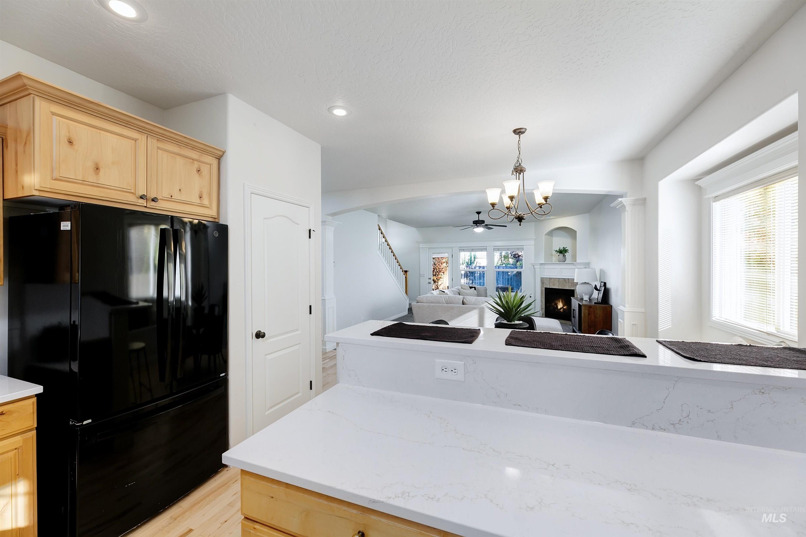 Kitchen with freestanding refrigerator, light brown cabinets, a lit fireplace, light stone counters, and open floor plan