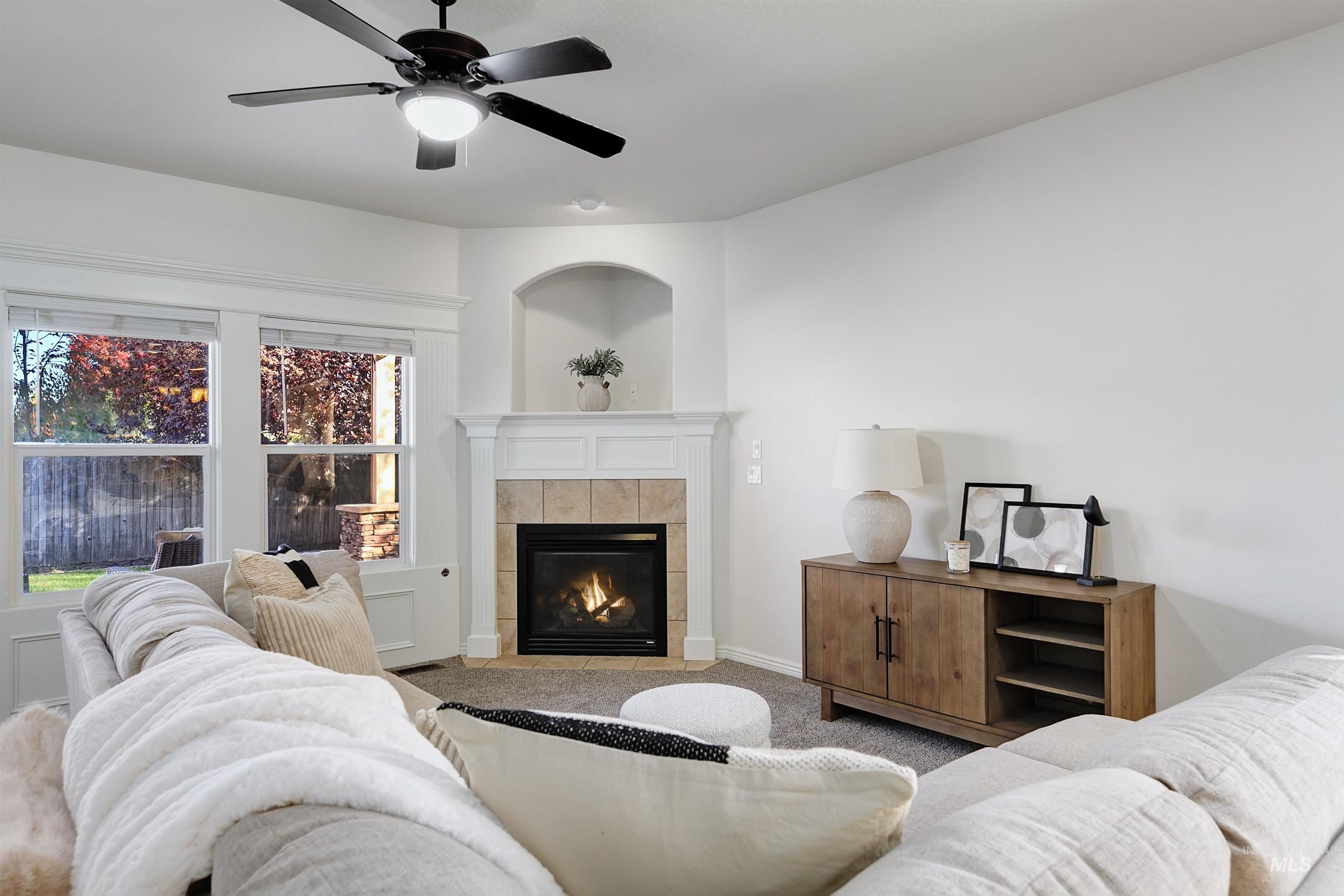 Carpeted living area featuring a tiled fireplace and ceiling fan