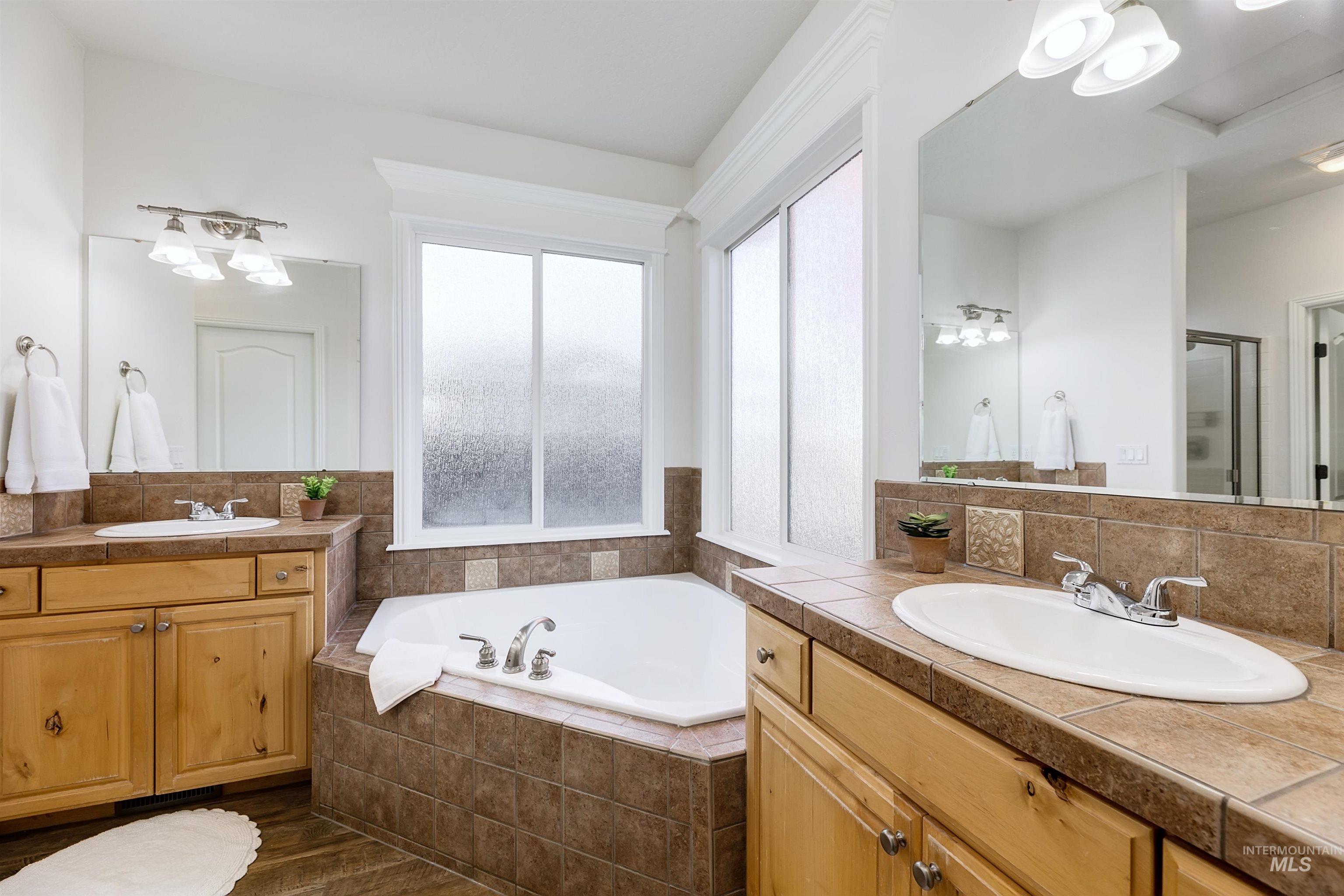 Full bath featuring a bath, two vanities, tasteful backsplash, and a stall shower