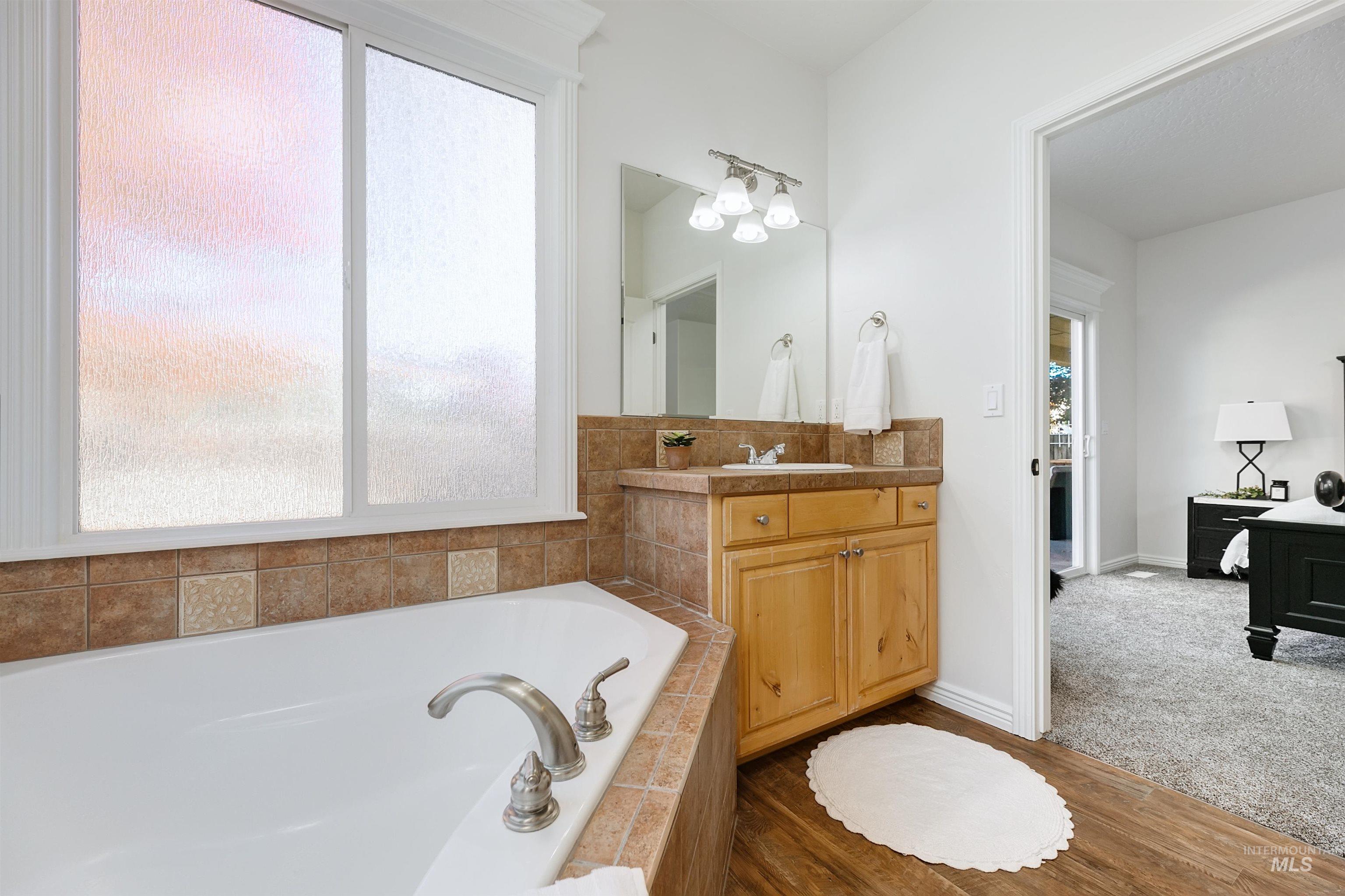 Bathroom featuring vanity, a garden tub, dark wood-style flooring, and dark colored carpet