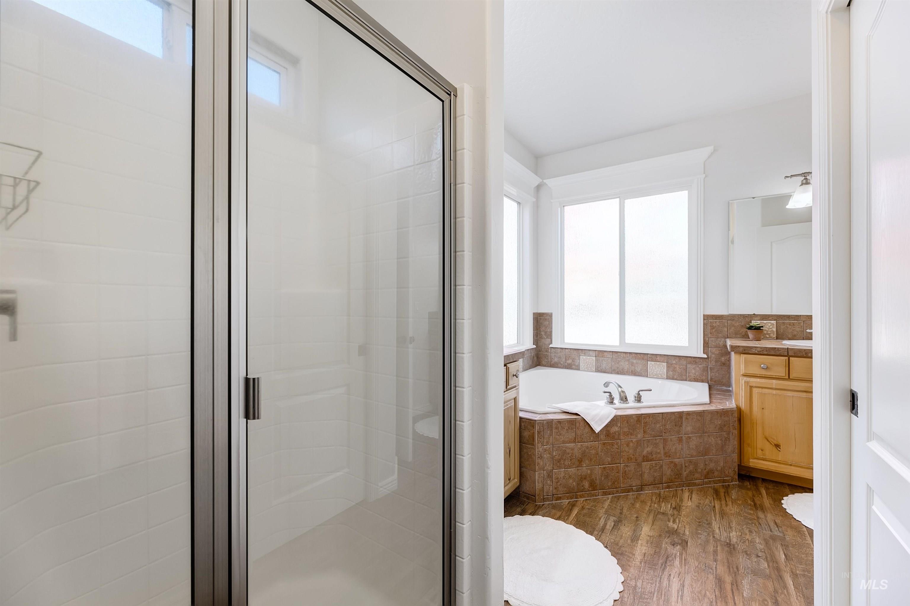 Full bathroom featuring dark wood-style flooring, vanity, a stall shower, and a garden tub