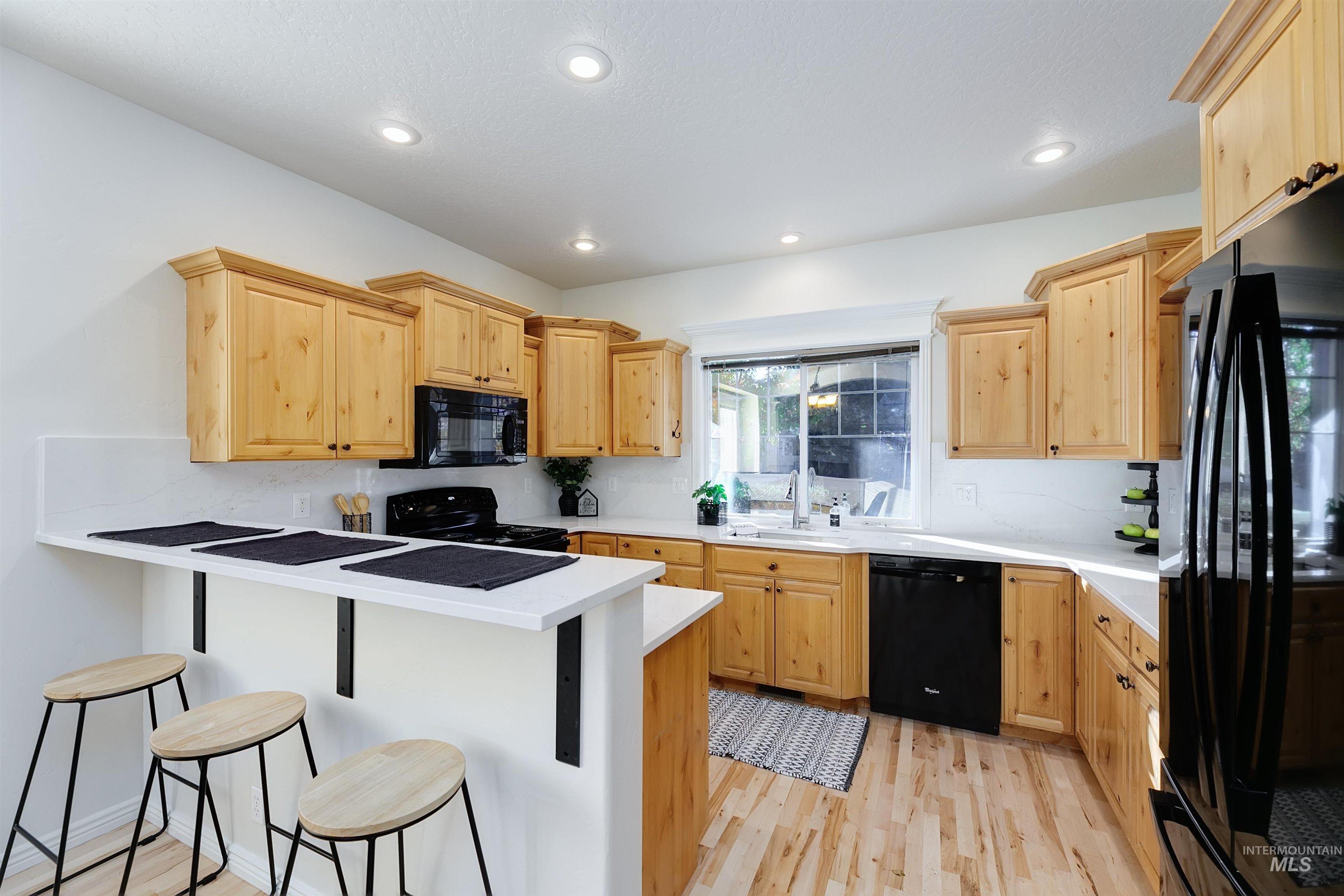 Kitchen featuring a breakfast bar area, light wood-style floors, light brown cabinetry, black appliances, and recessed lighting