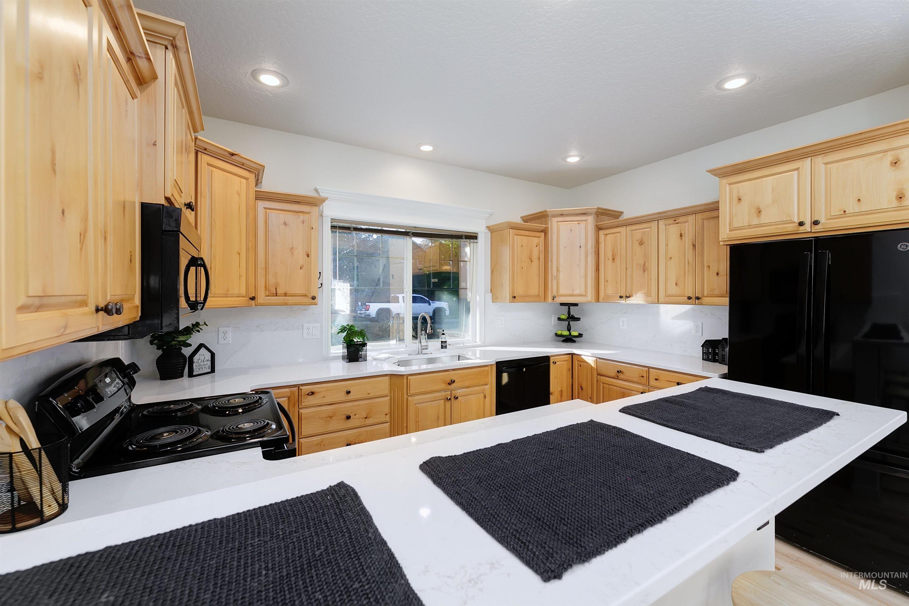 Kitchen featuring light brown cabinets, black appliances, recessed lighting, and light stone countertops