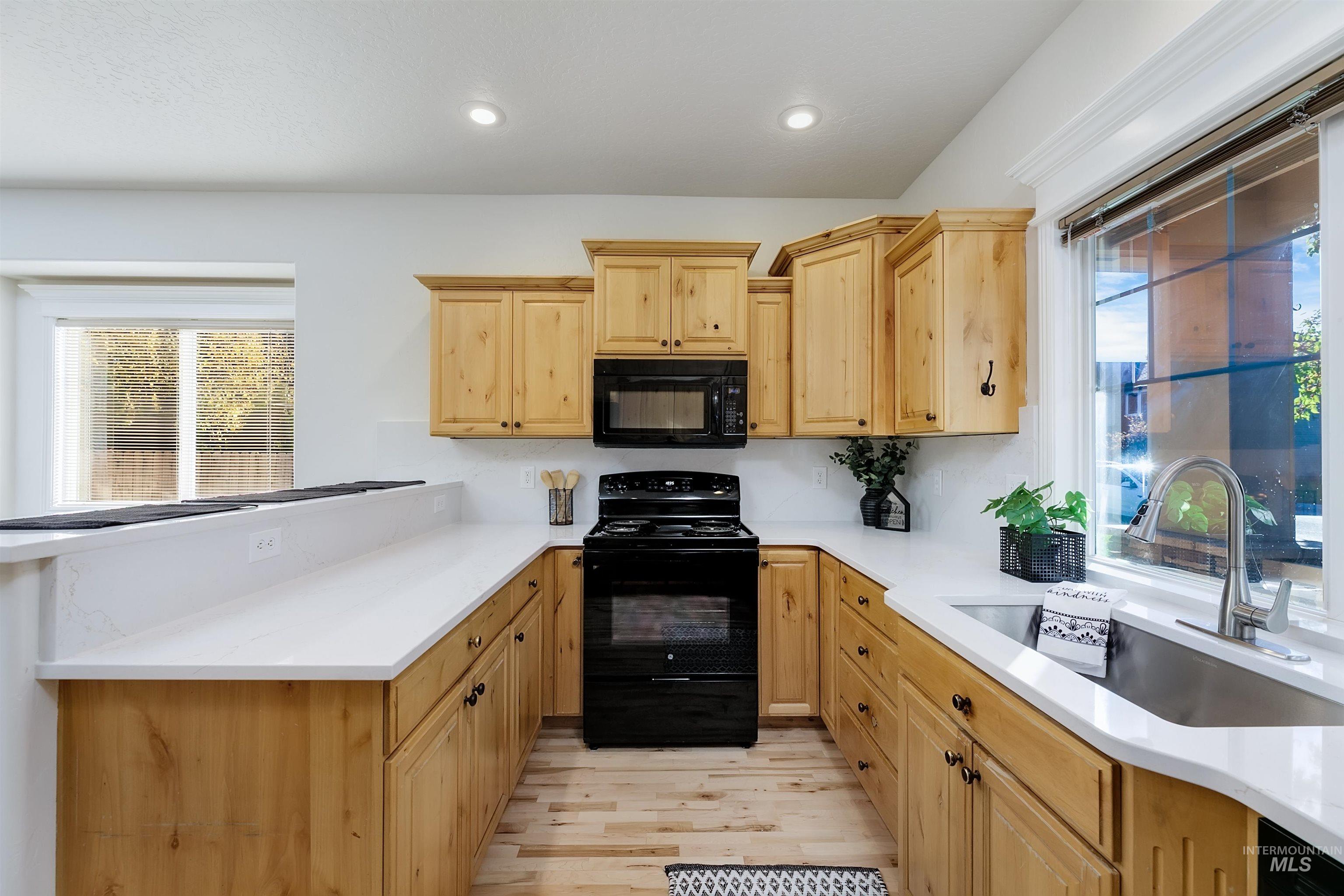 Kitchen with black appliances, light brown cabinetry, light wood-style floors, recessed lighting, and a peninsula