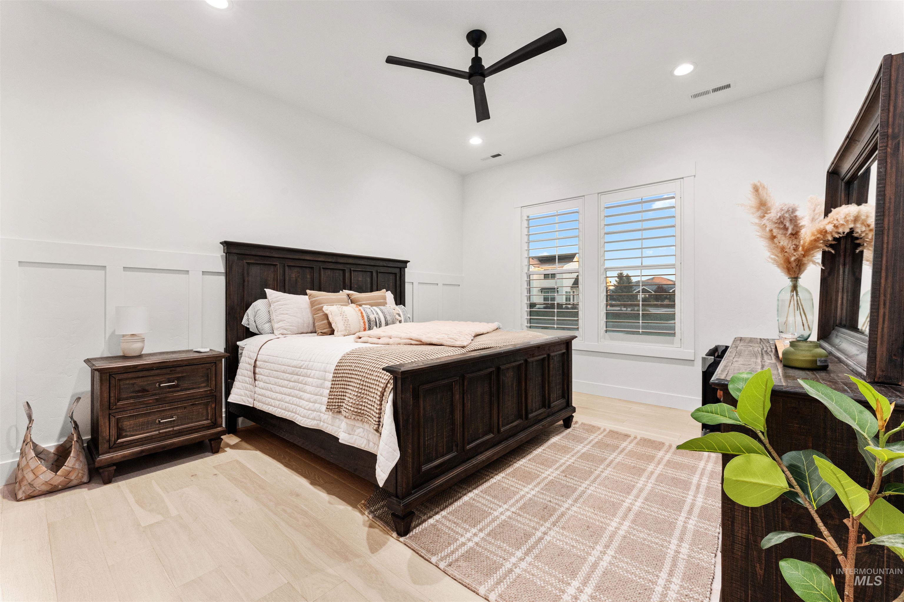 Bedroom with light wood-style floors, a ceiling fan, recessed lighting, and a decorative wall