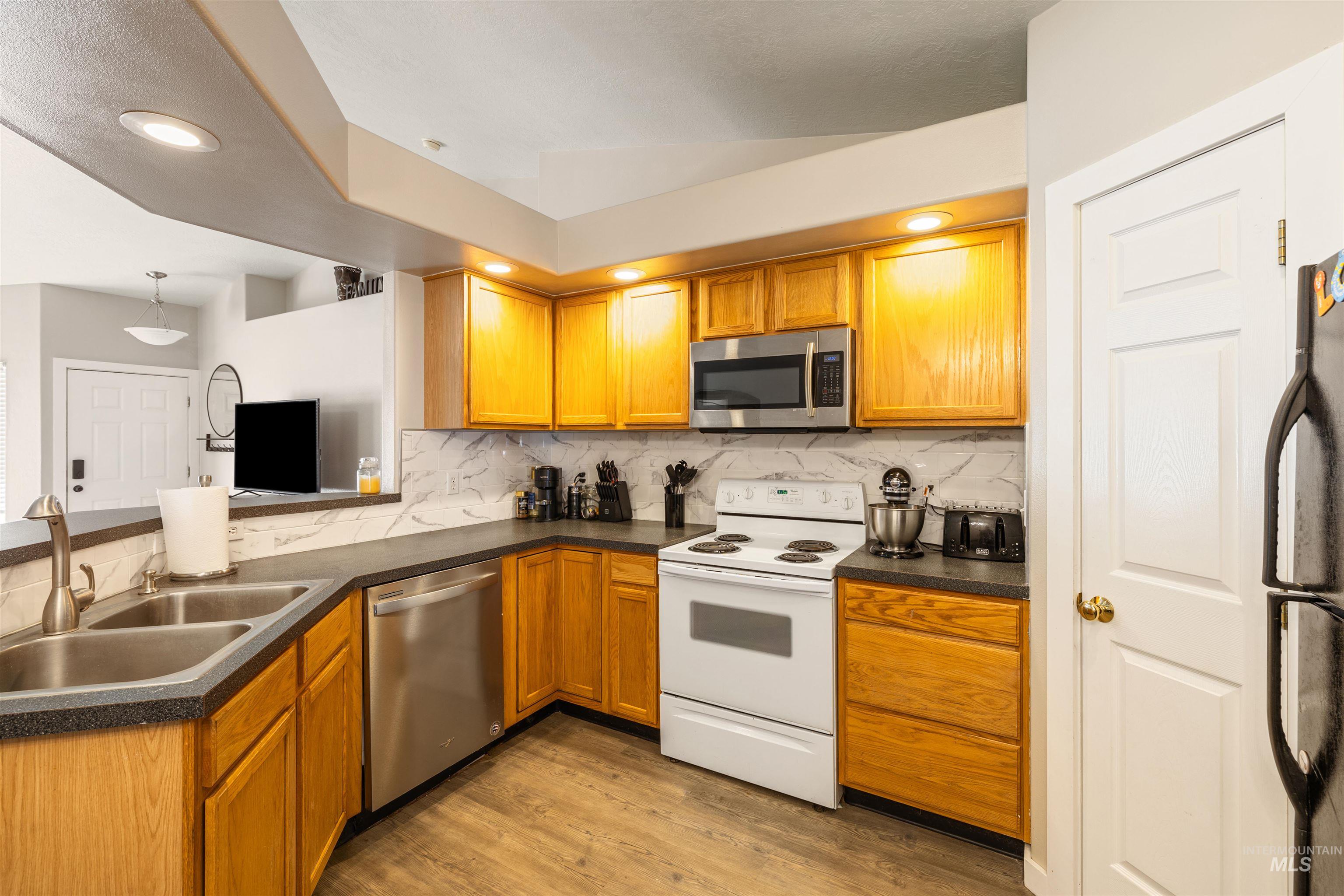 Kitchen with stainless steel appliances, dark countertops, decorative backsplash, brown cabinetry, and light wood-style floors