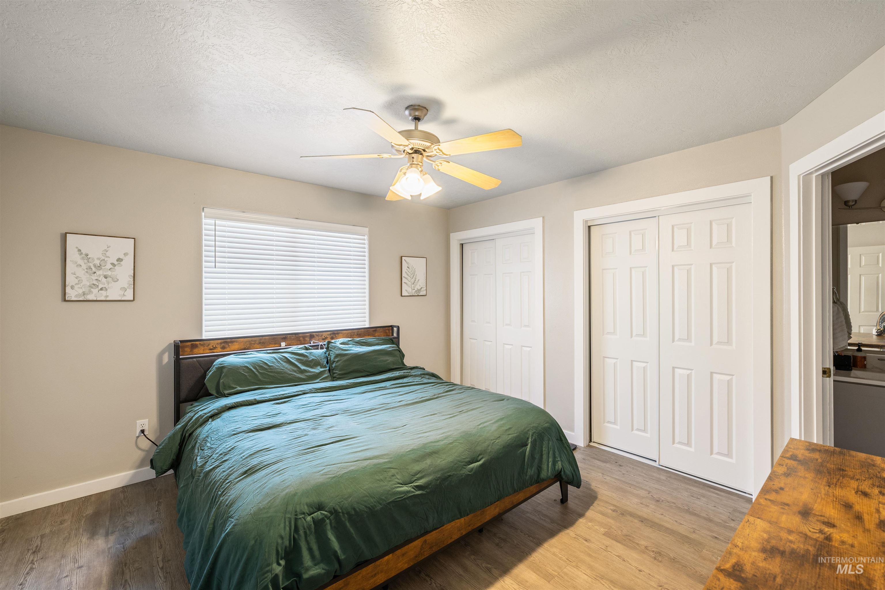 Bedroom with two closets, a textured ceiling, light wood-style flooring, and ceiling fan