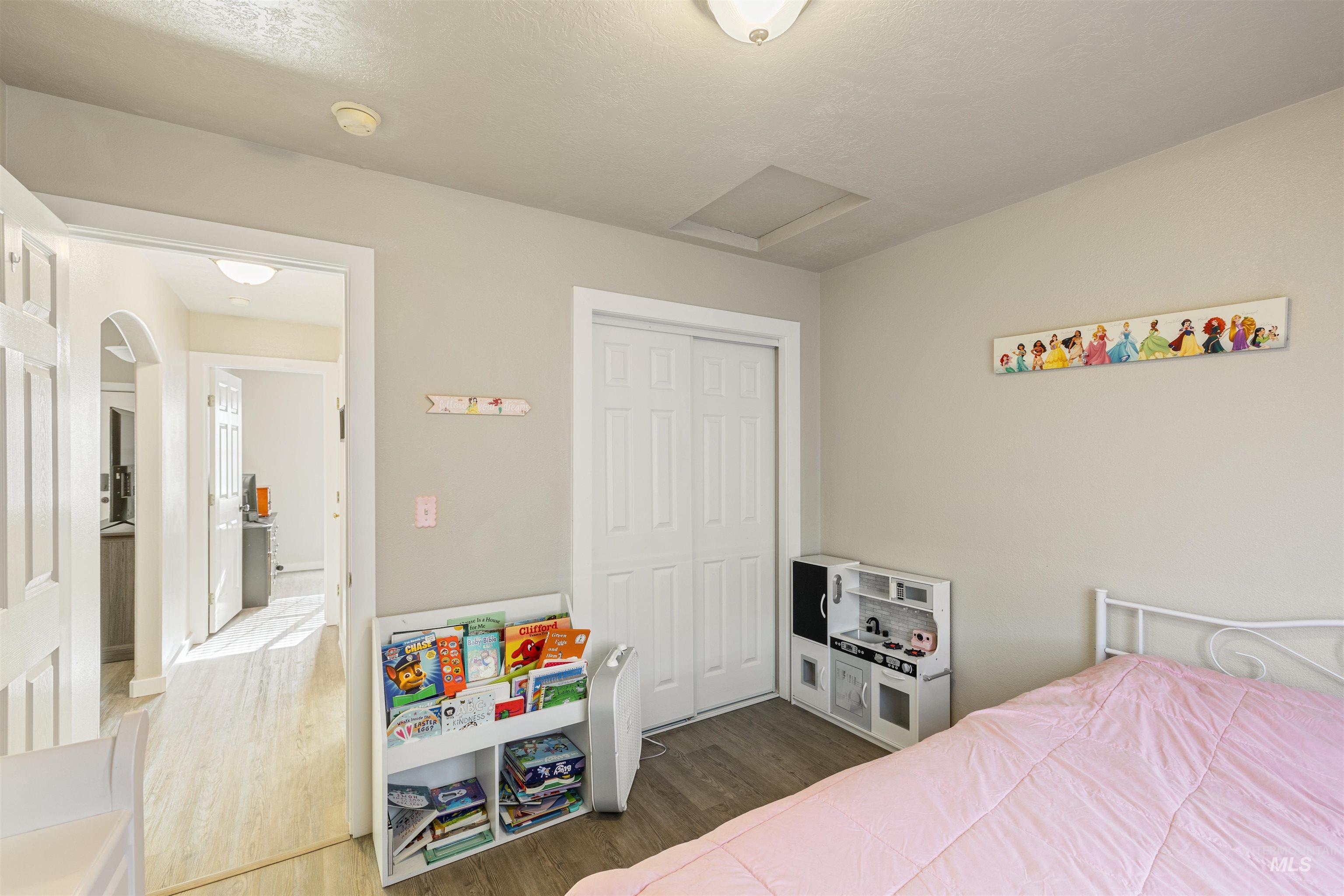 Bedroom featuring wood finished floors, attic access, a closet, and a textured ceiling