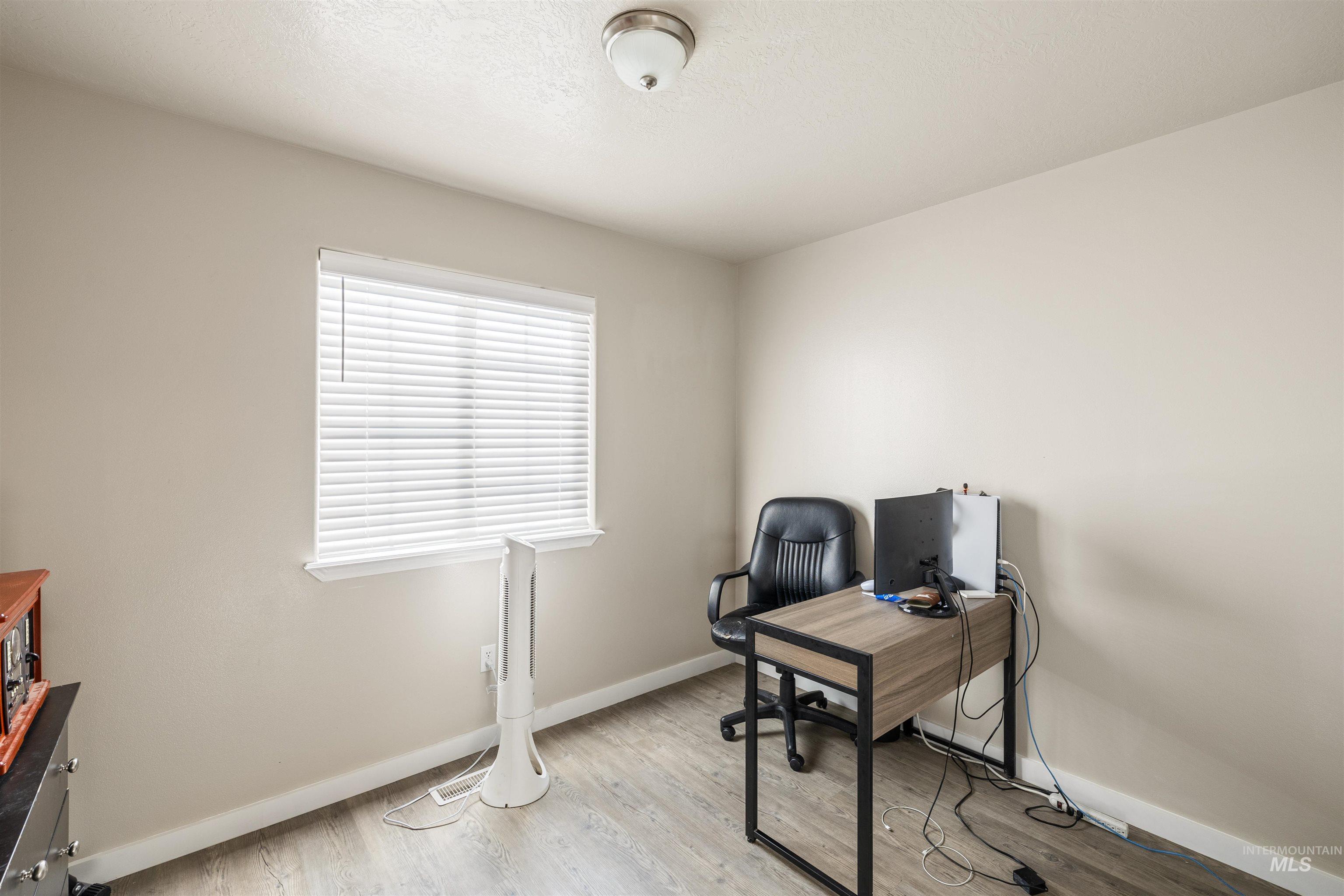 Home office with light wood-style floors and a textured ceiling