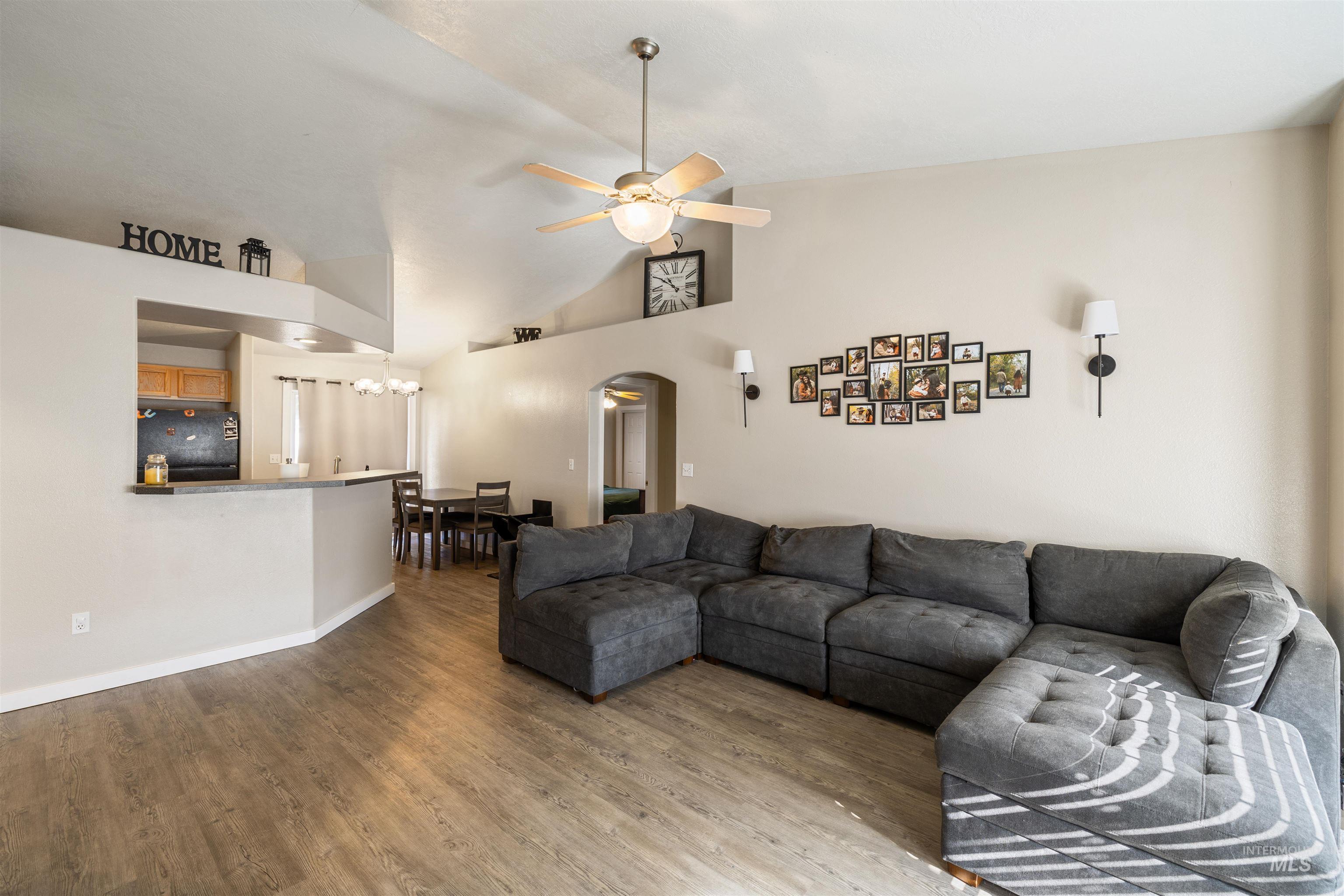 Living room featuring a ceiling fan, wood finished floors, high vaulted ceiling, arched walkways, and a chandelier