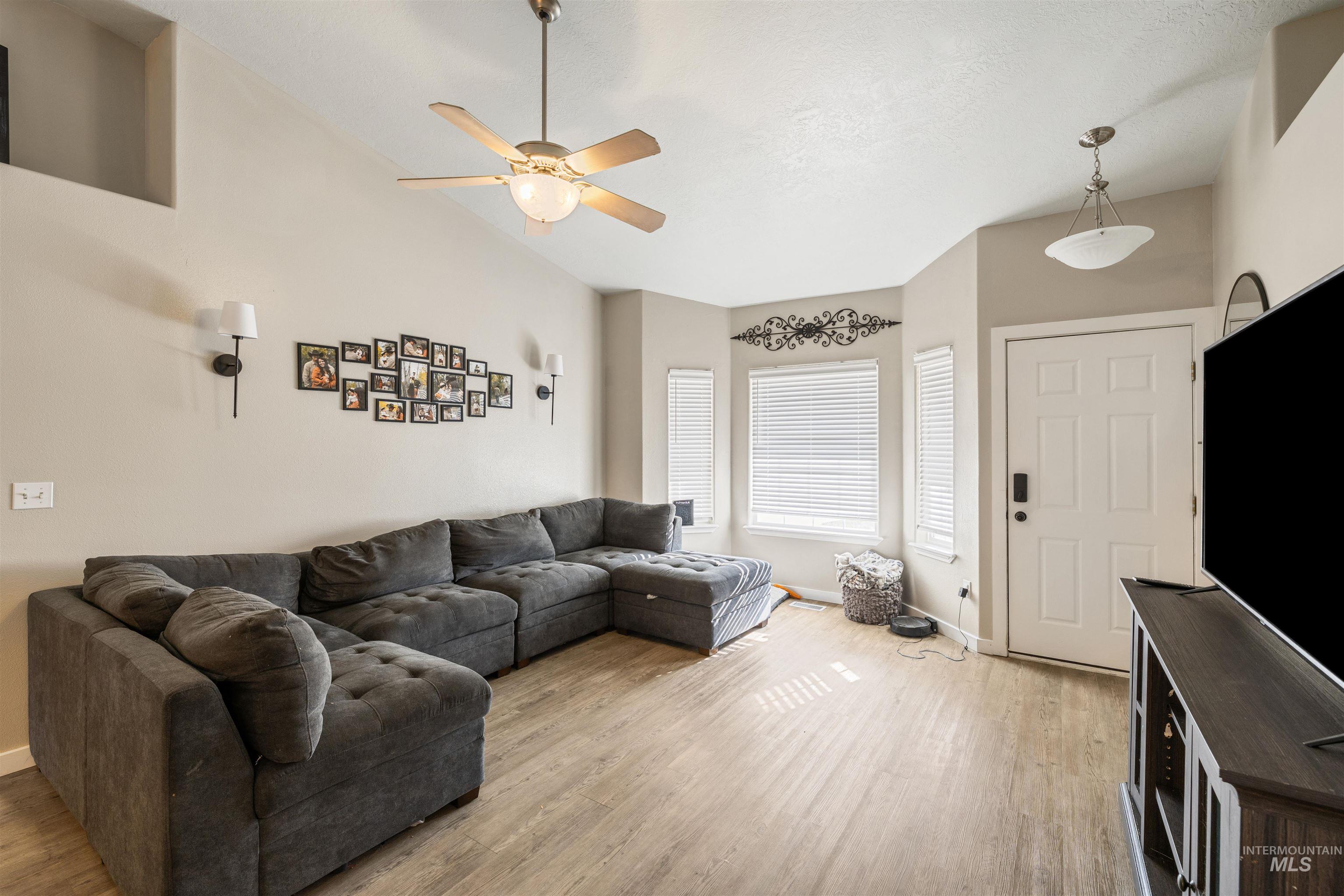 Living area with ceiling fan, wood finished floors, and high vaulted ceiling