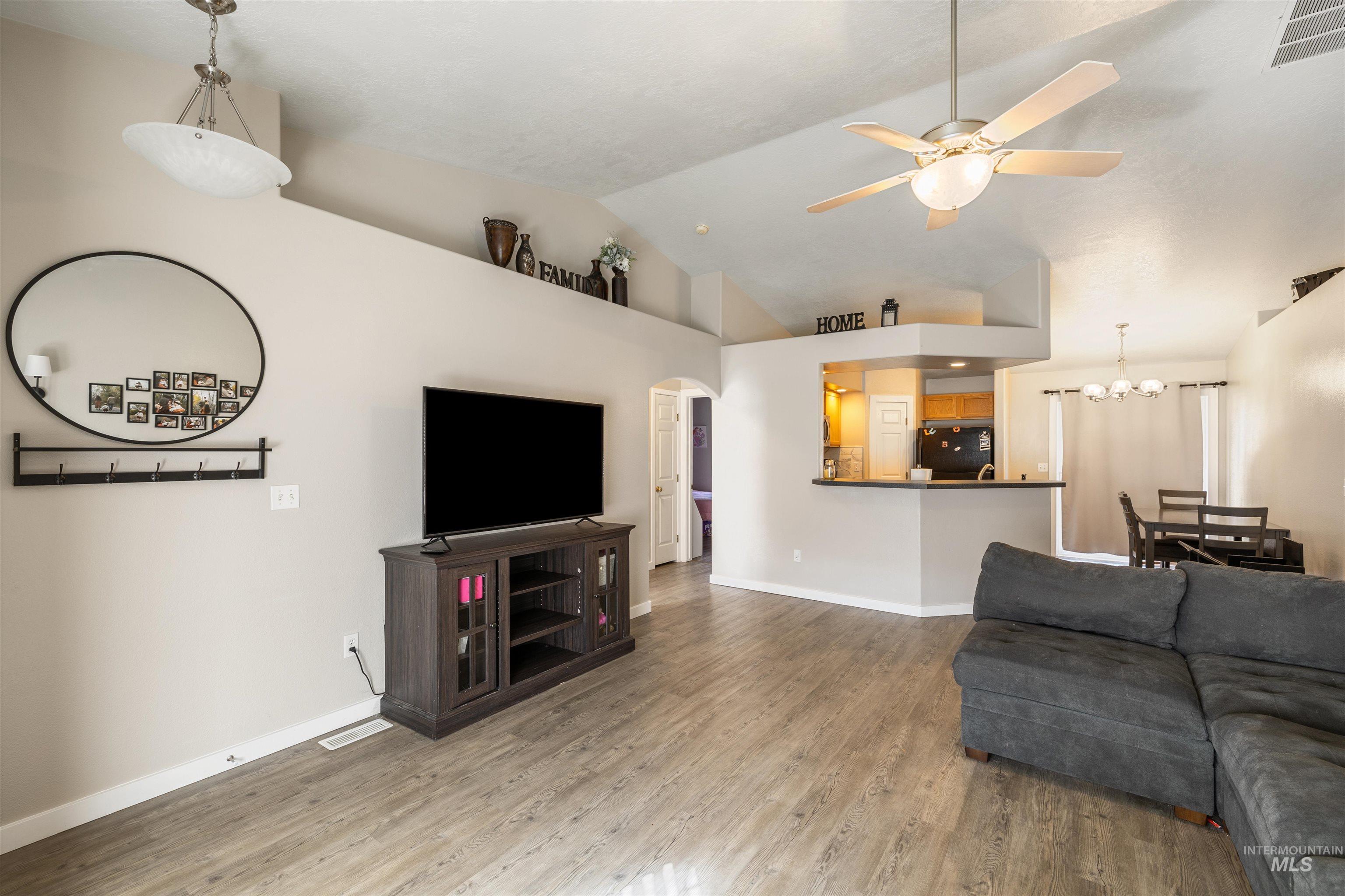 Living area with wood finished floors, a ceiling fan, arched walkways, a chandelier, and high vaulted ceiling