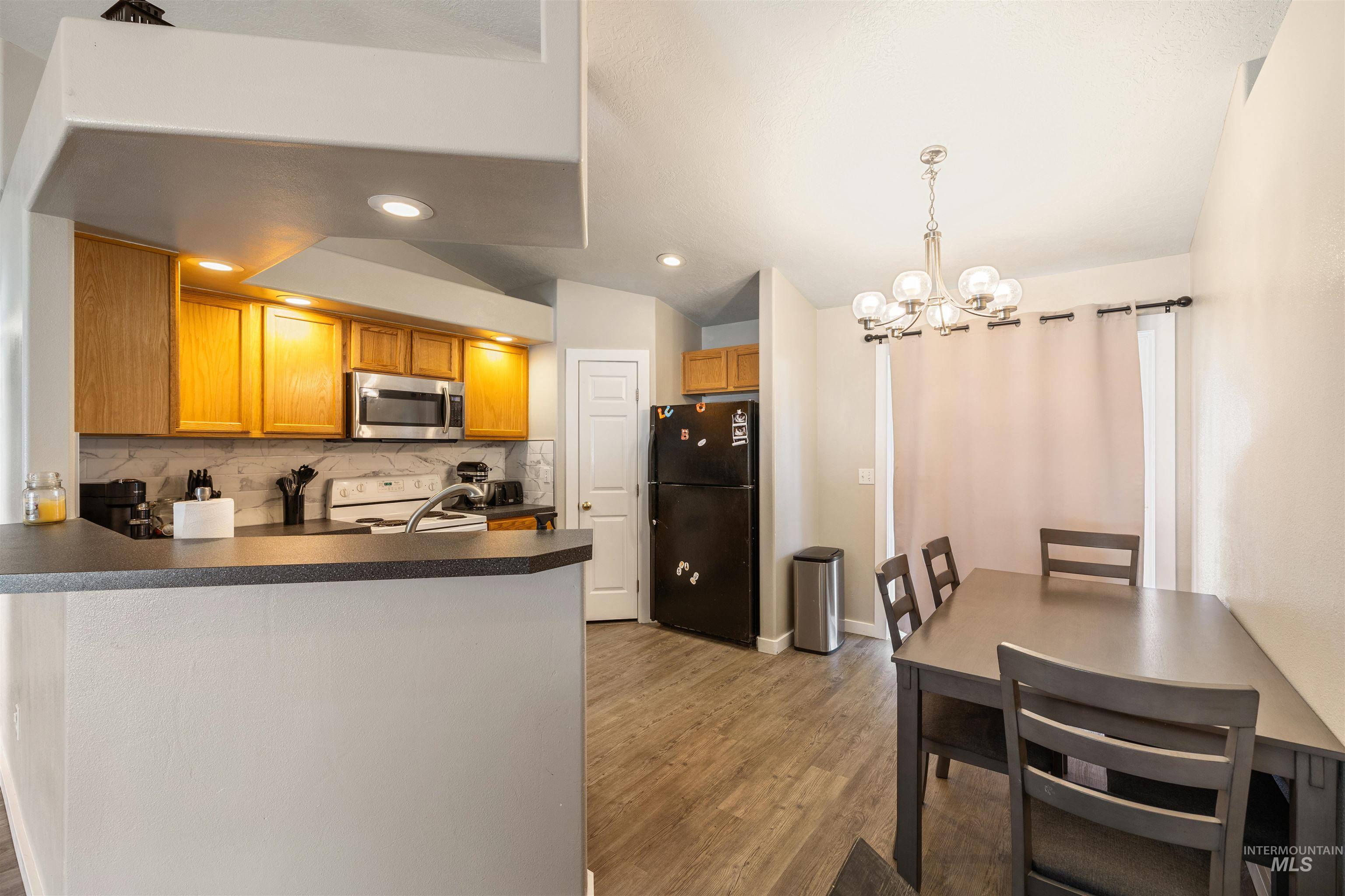 Kitchen with brown cabinets, freestanding refrigerator, decorative backsplash, white range with electric cooktop, and light wood-style floors