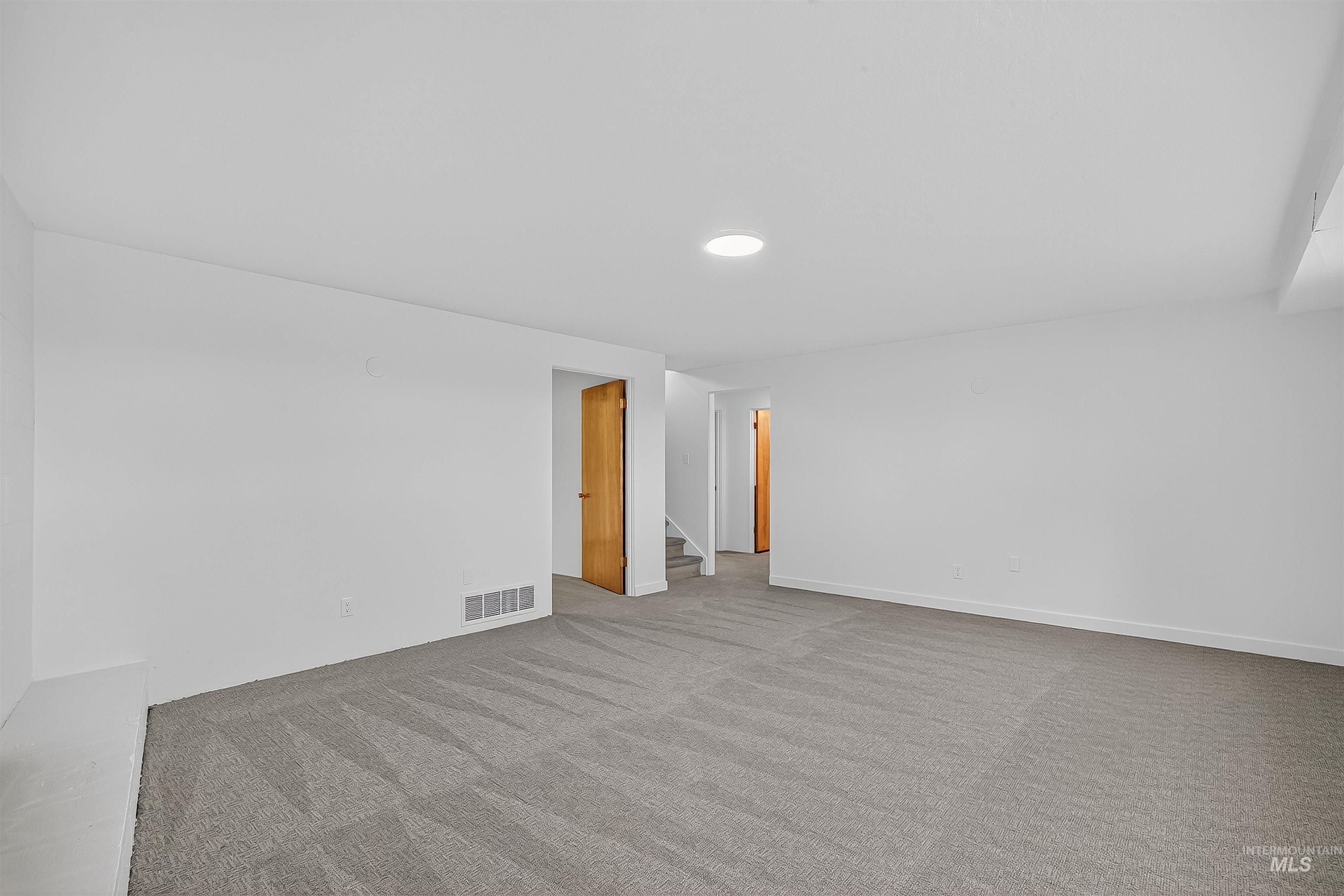 Carpeted spare room featuring stairs and baseboards