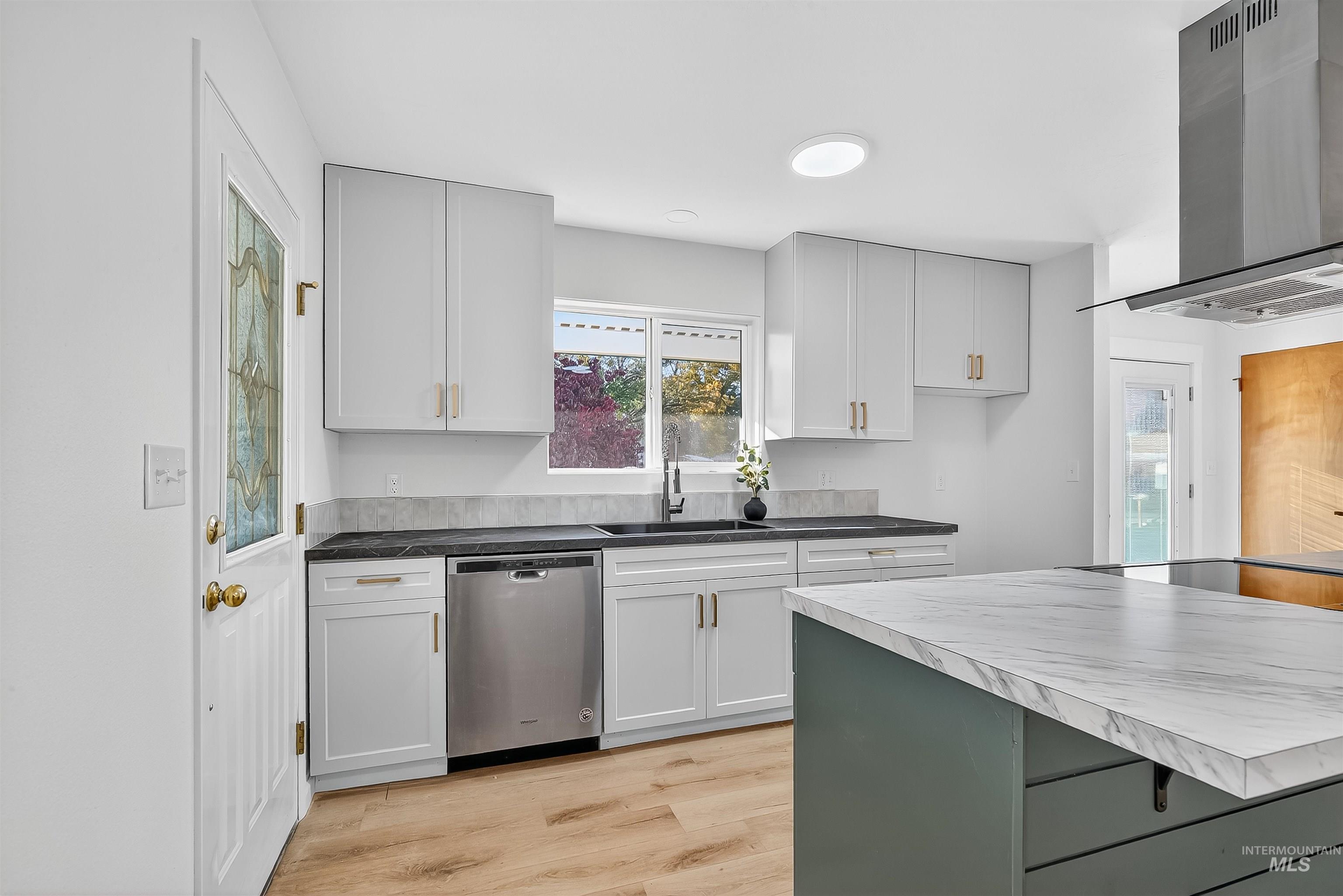 Kitchen with wall chimney range hood, stainless steel dishwasher, light wood-type flooring, white cabinets, and a kitchen bar