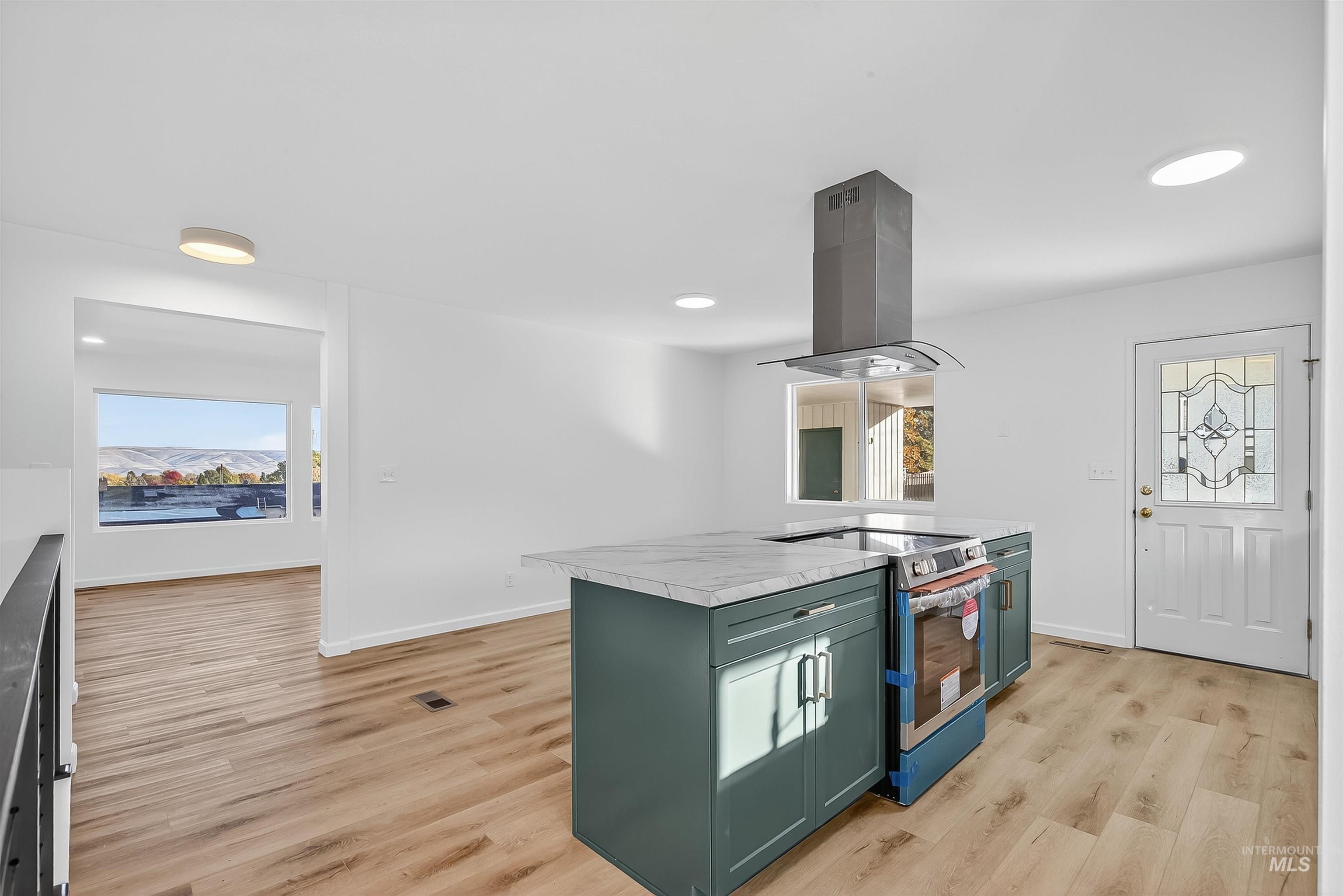 Kitchen featuring green cabinetry, electric stove, light countertops, light wood finished floors, and island range hood