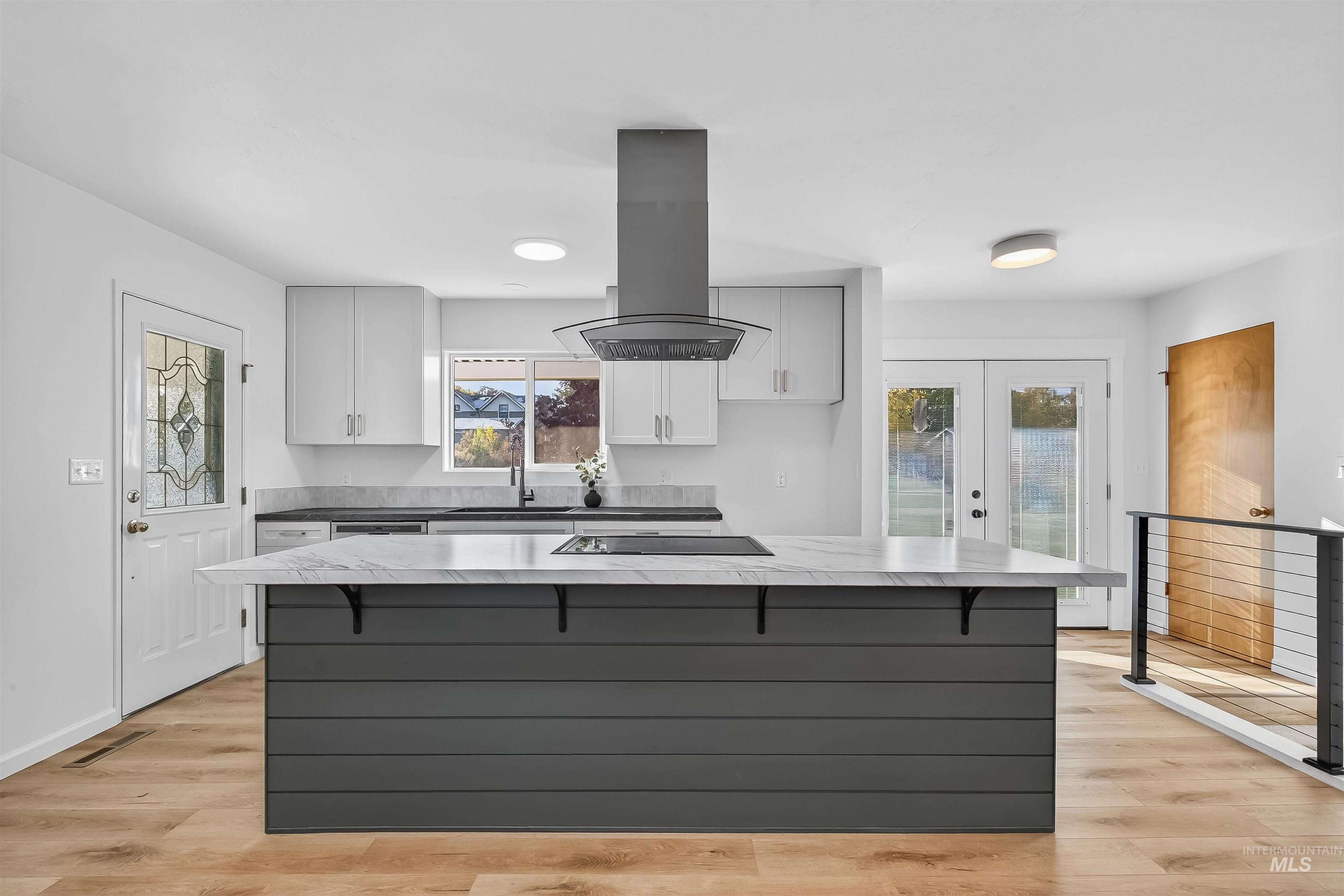 Kitchen with white cabinets, light countertops, gray cabinetry, island exhaust hood, and a breakfast bar