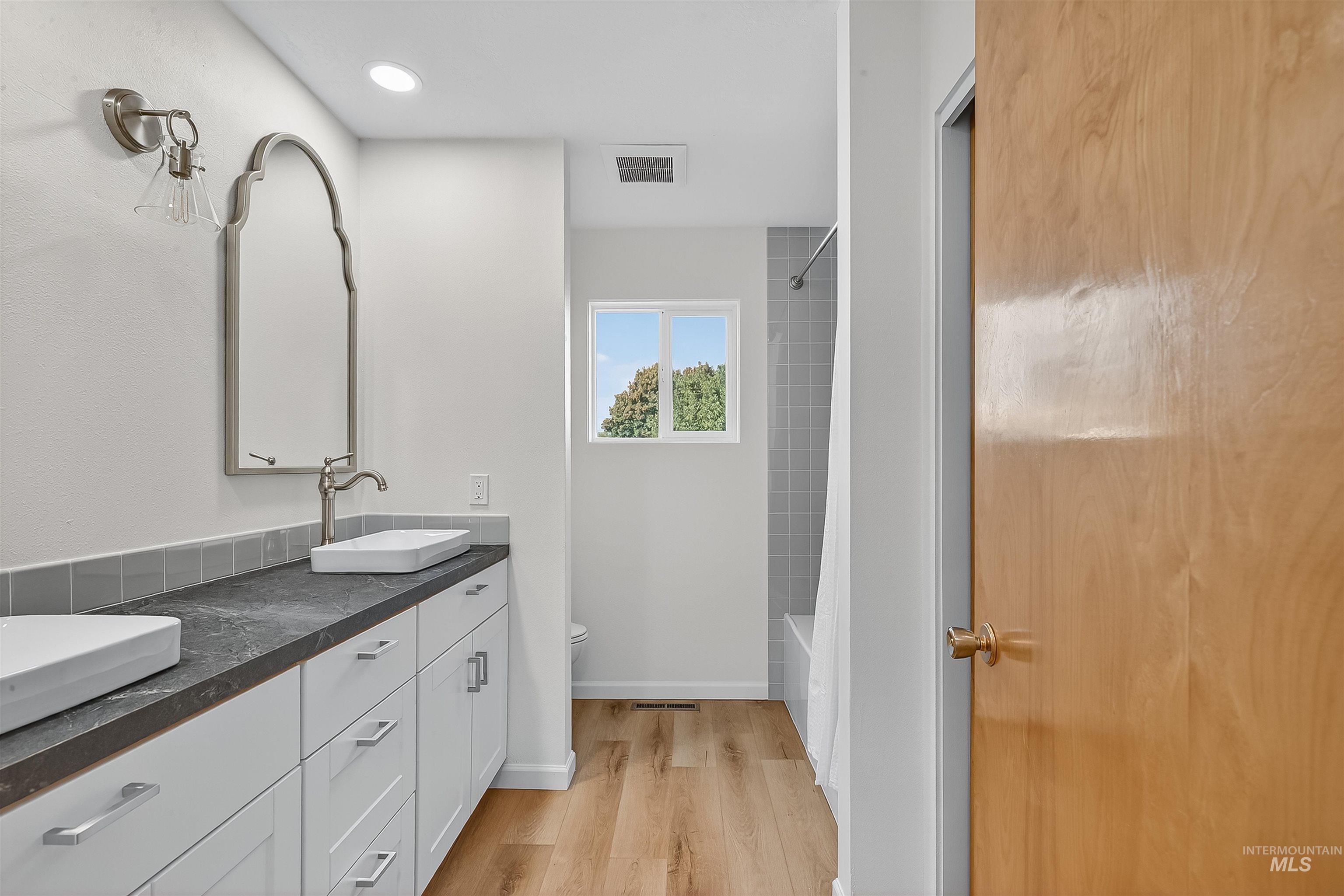 Full bathroom featuring double vanity, light wood finished floors, and shower / tub combo