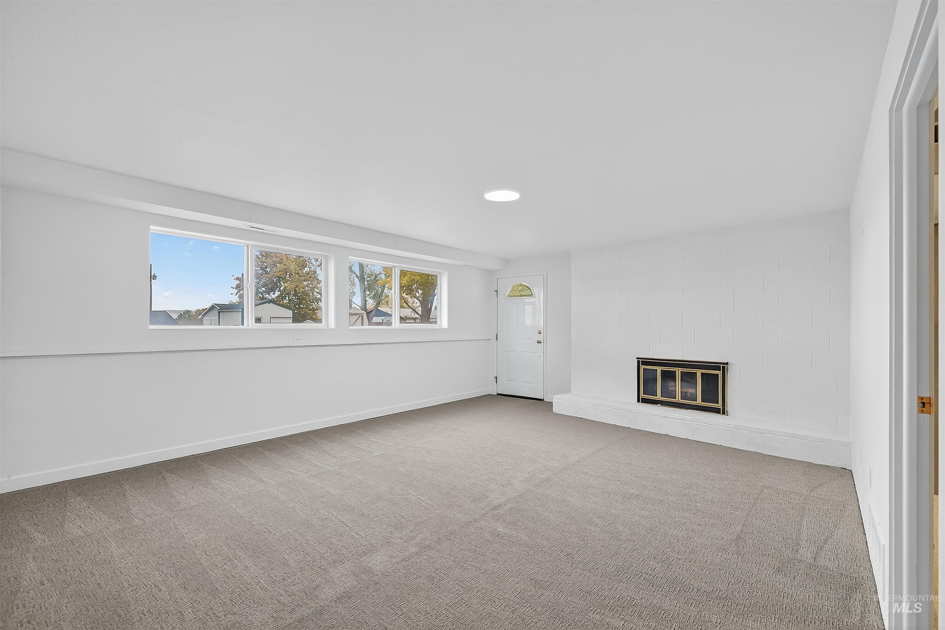 Unfurnished living room featuring a glass covered fireplace and light colored carpet