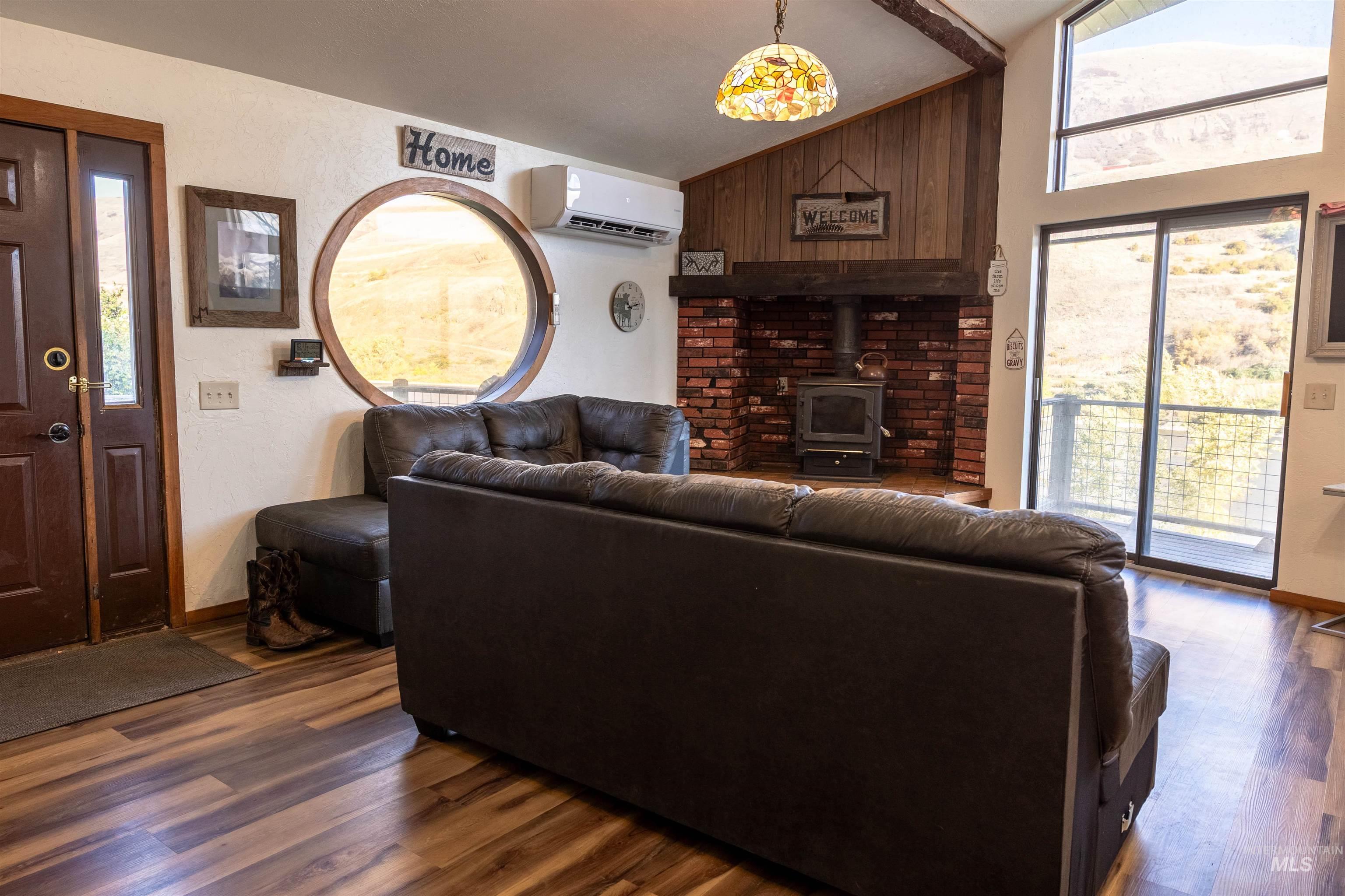 Living area with a wood stove, lofted ceiling, dark wood-style floors, and a wall mounted air conditioner