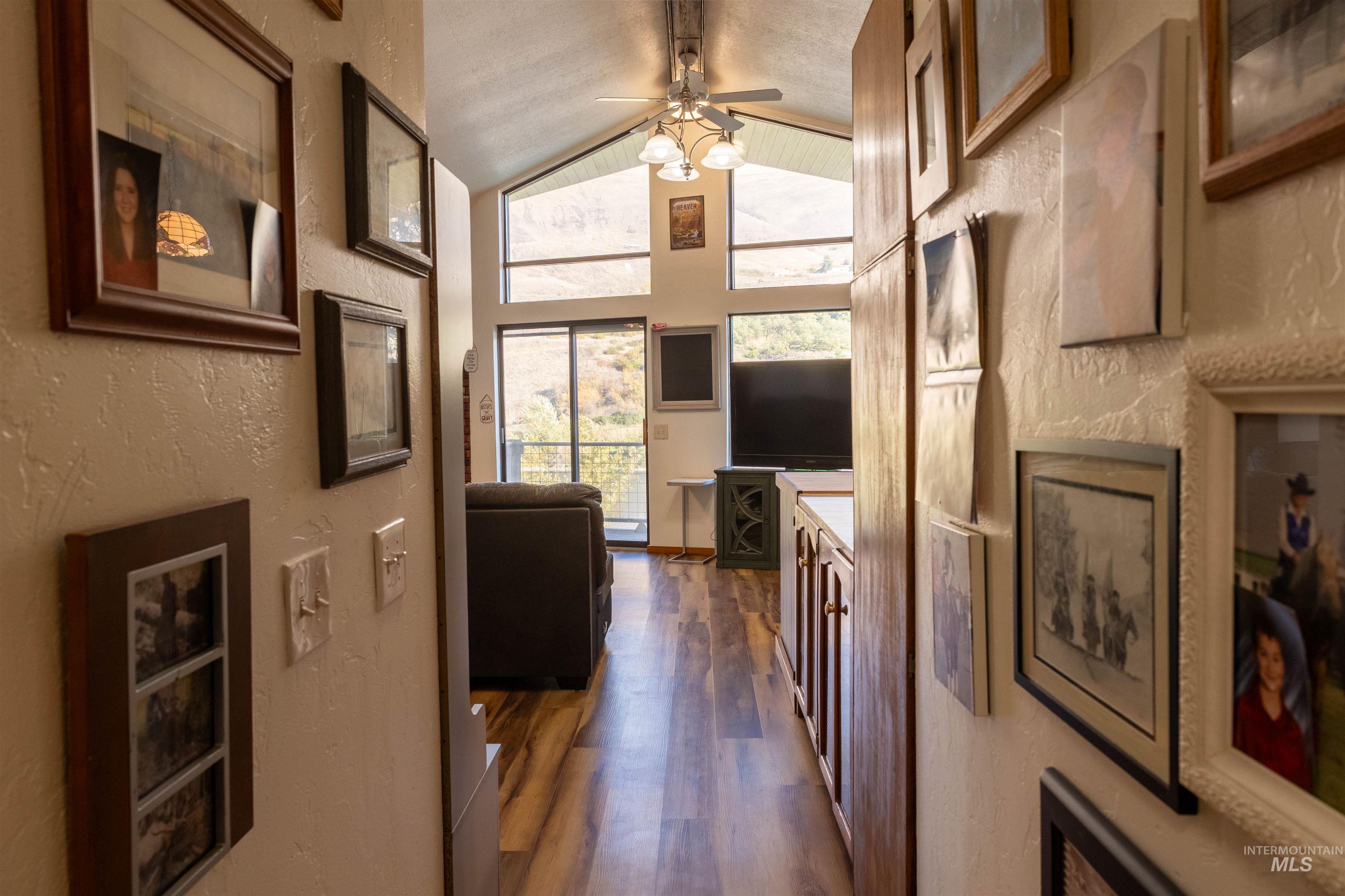 Living area featuring a textured wall, dark wood finished floors, a ceiling fan, and high vaulted ceiling