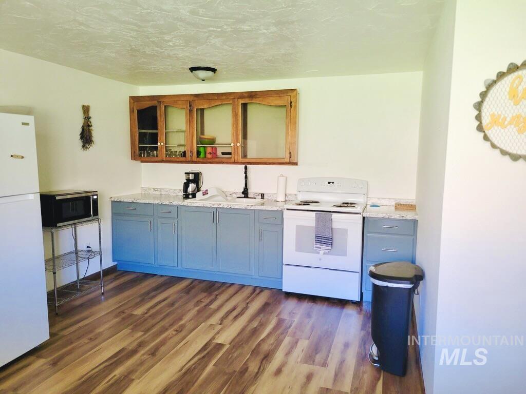 Kitchen featuring white appliances, dark wood-type flooring, glass insert cabinets, a textured ceiling, and light stone counters
