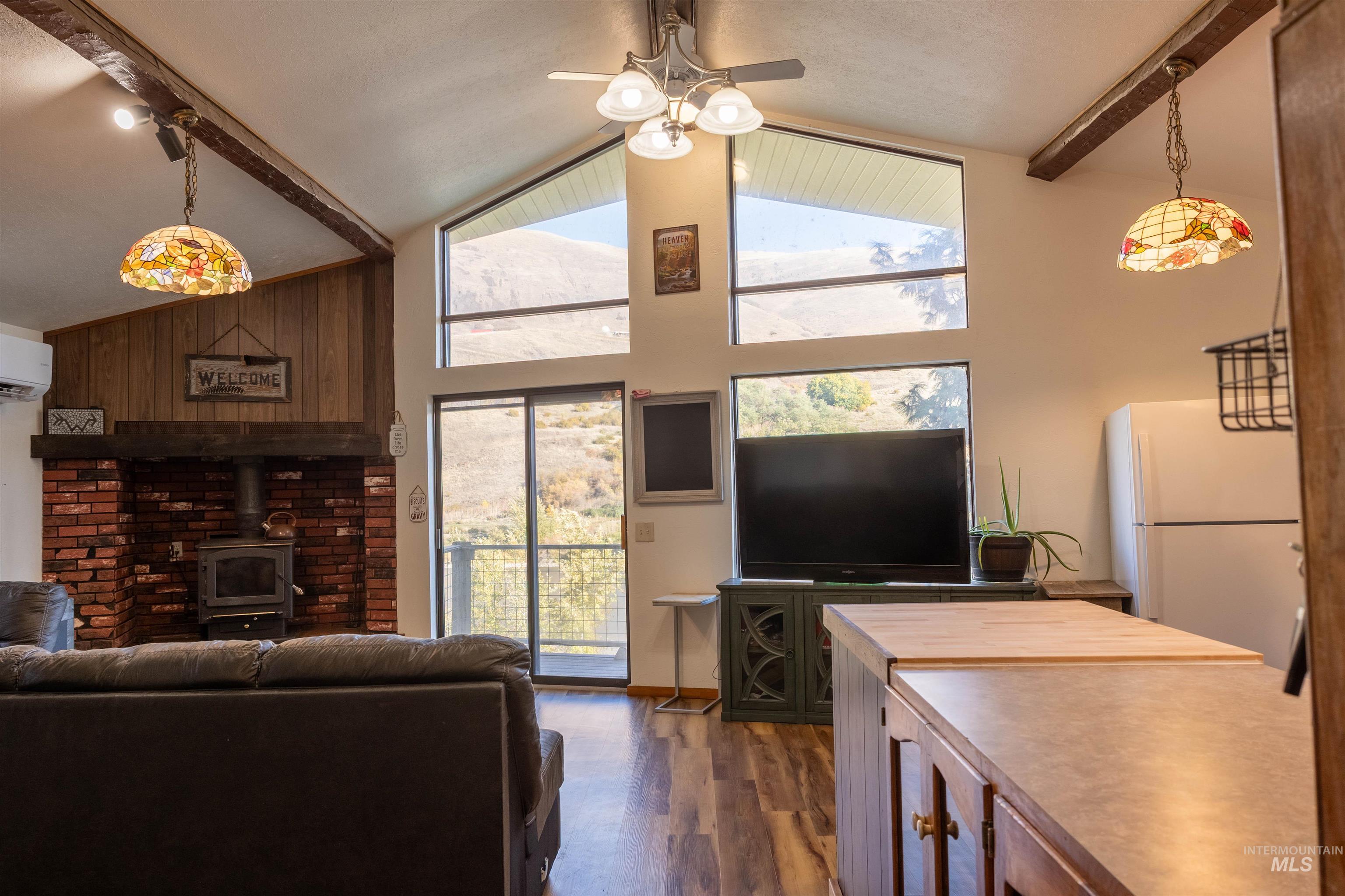 Living room featuring beamed ceiling, a wood stove, dark wood-style flooring, high vaulted ceiling, and a ceiling fan