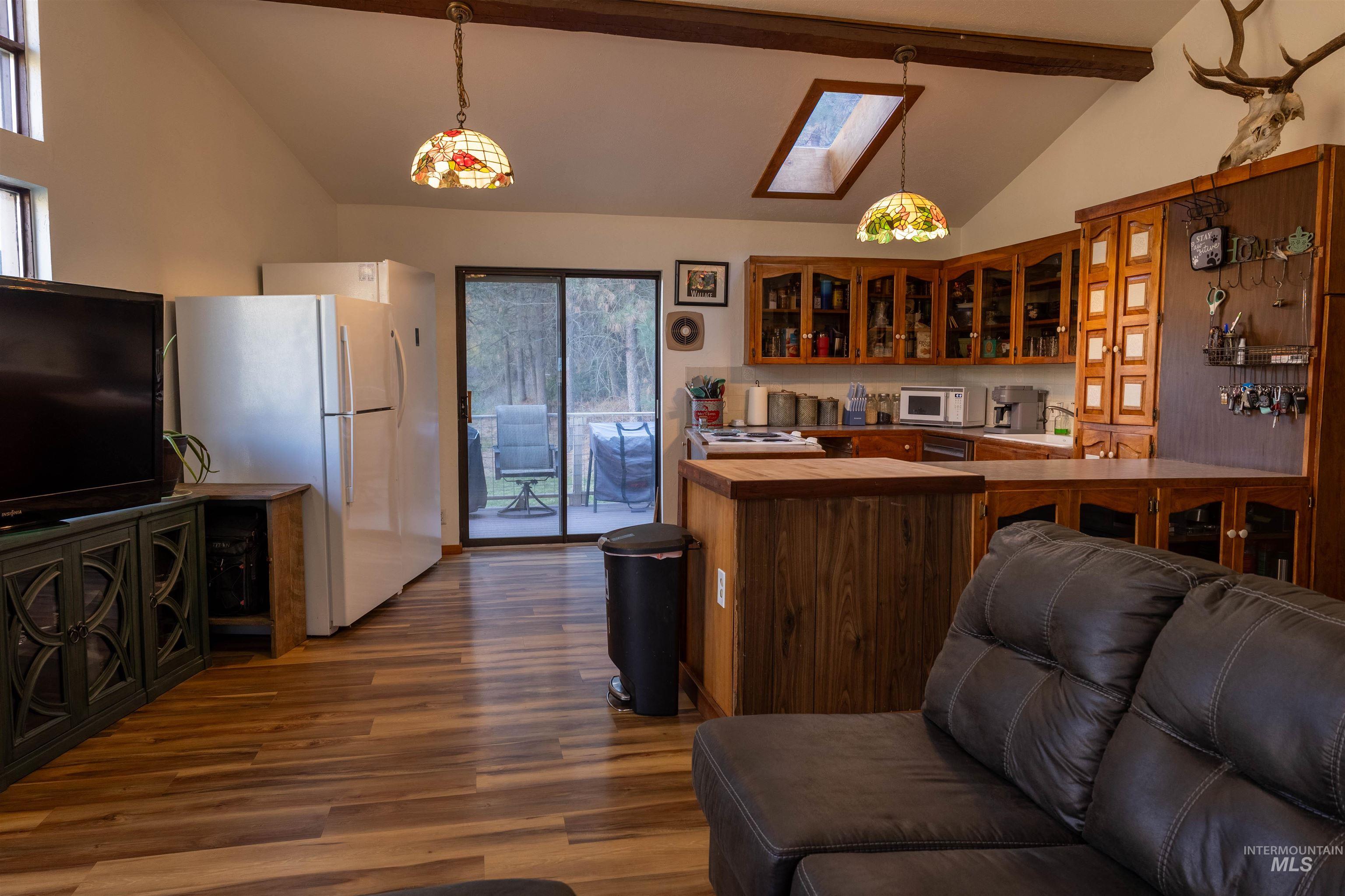 Kitchen featuring glass insert cabinets, beamed ceiling, a skylight, brown cabinets, and high vaulted ceiling