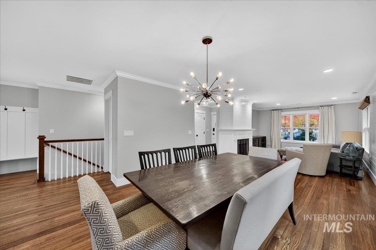 Dining area with crown molding, dark wood-style floors, a fireplace, a chandelier, and recessed lighting