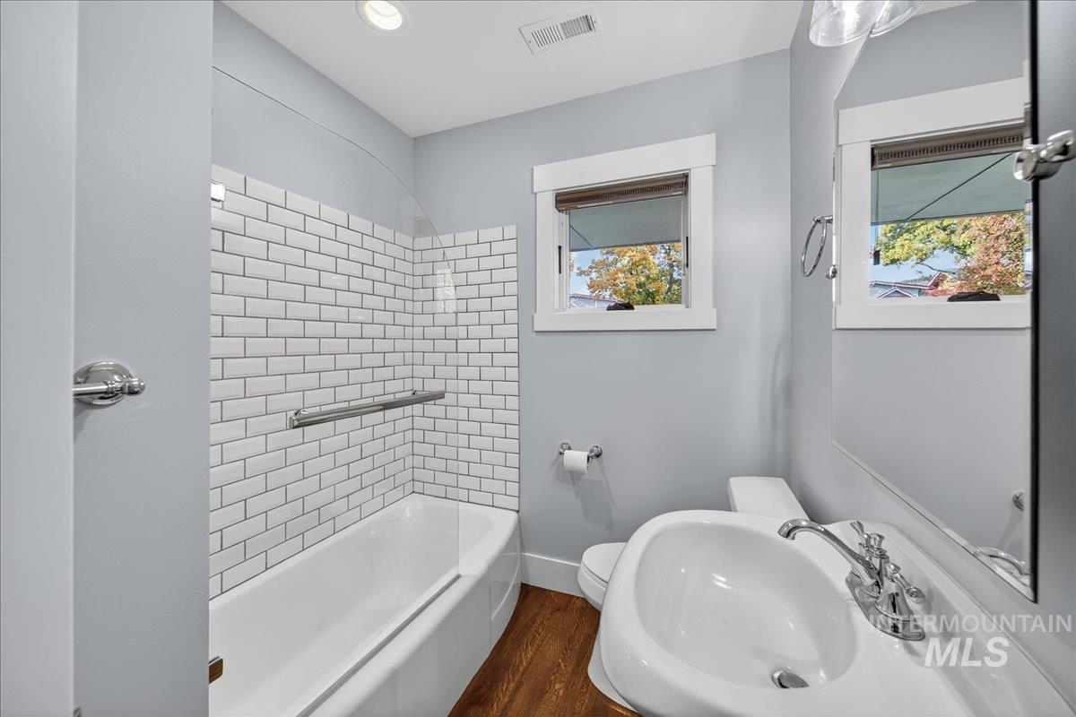 Bathroom with dark wood-type flooring, bathtub / shower combination, and recessed lighting