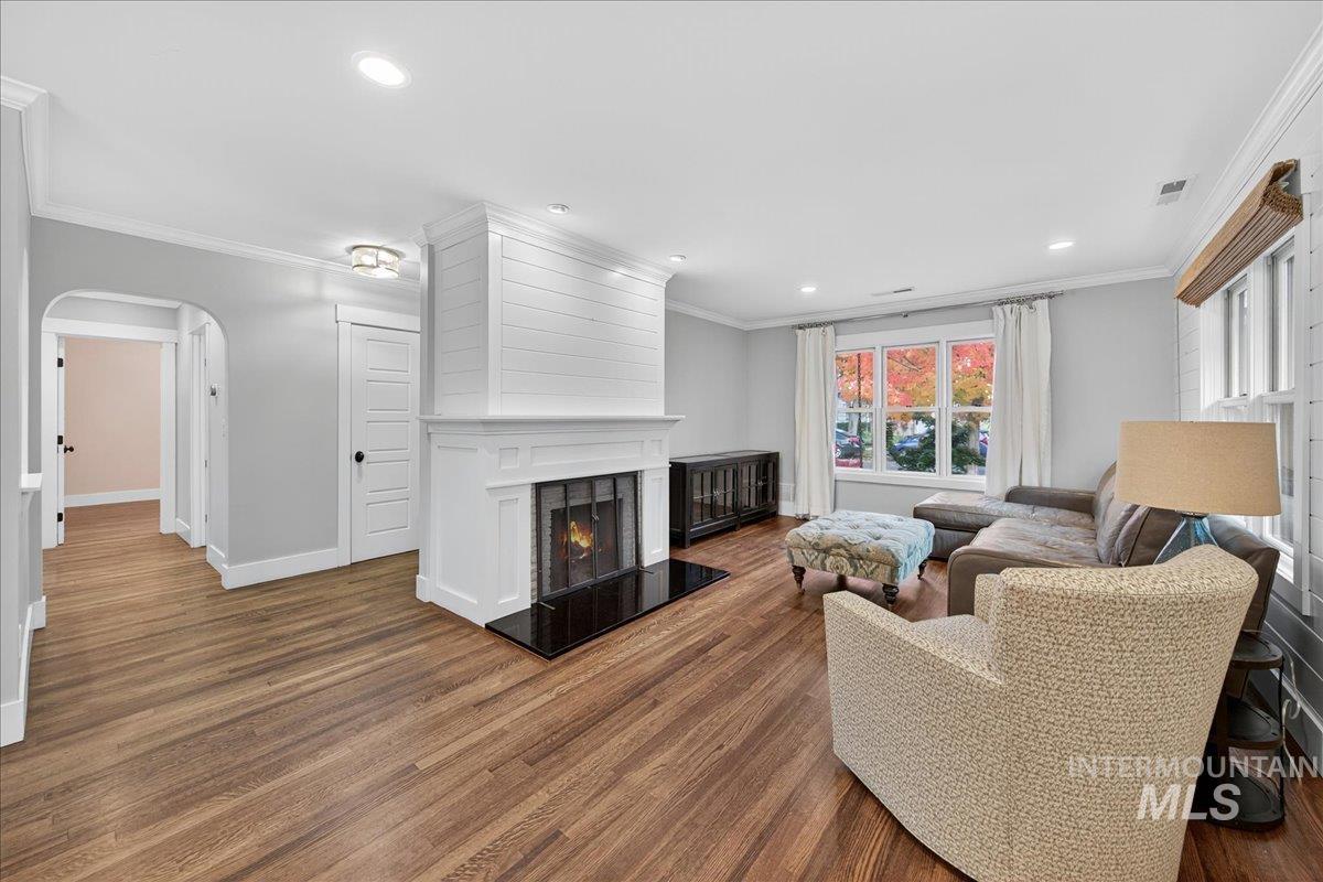 Living room with arched walkways, a large fireplace, ornamental molding, dark wood-type flooring, and recessed lighting