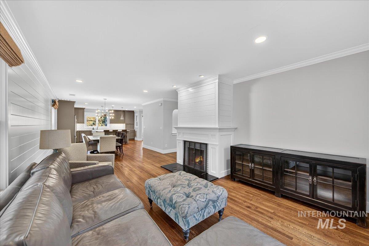Living room featuring ornamental molding, wood finished floors, a warm lit fireplace, recessed lighting, and a chandelier