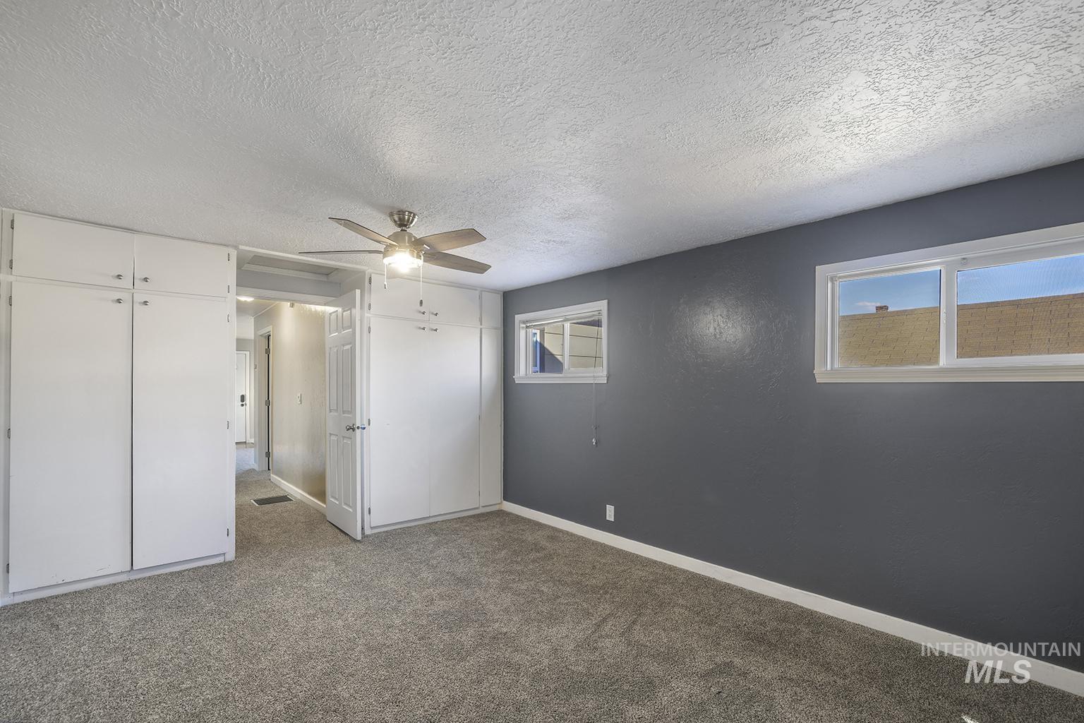 Unfurnished bedroom with carpet, a textured ceiling, a ceiling fan, and two closets