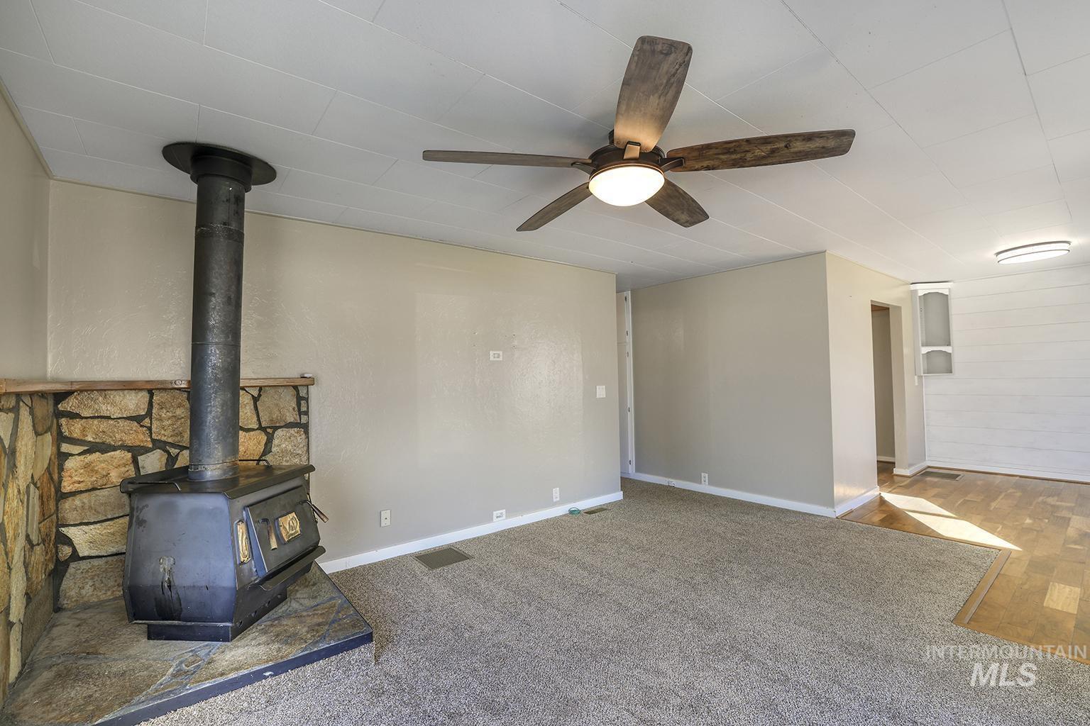 Unfurnished living room with a wood stove, carpet, and ceiling fan