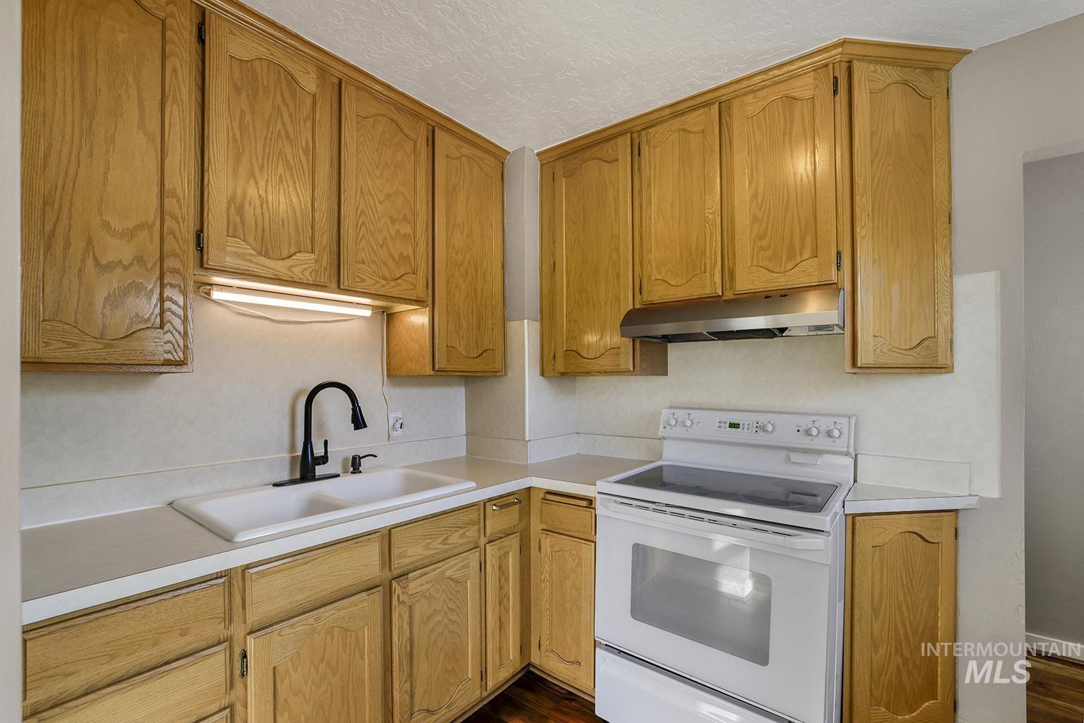 Kitchen with white electric range oven, light countertops, under cabinet range hood, dark wood-style floors, and a textured ceiling