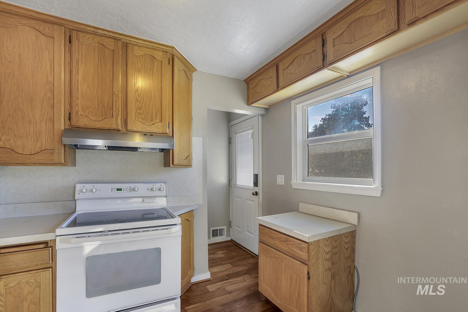 Kitchen with white electric range, light countertops, dark wood-type flooring, under cabinet range hood, and brown cabinetry