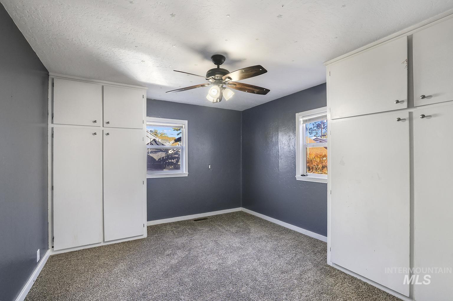 Unfurnished bedroom featuring light carpet, a ceiling fan, multiple windows, a textured ceiling, and a closet